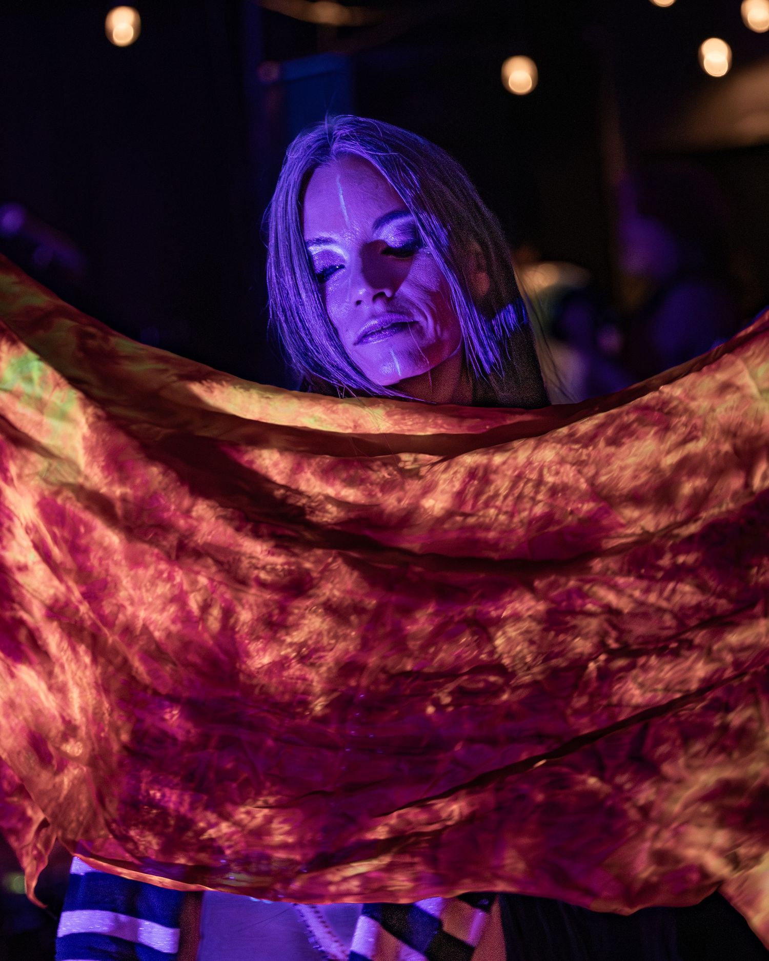 Woman performer holding colorful tie-dye fabric under purple stage lighting at live music event.