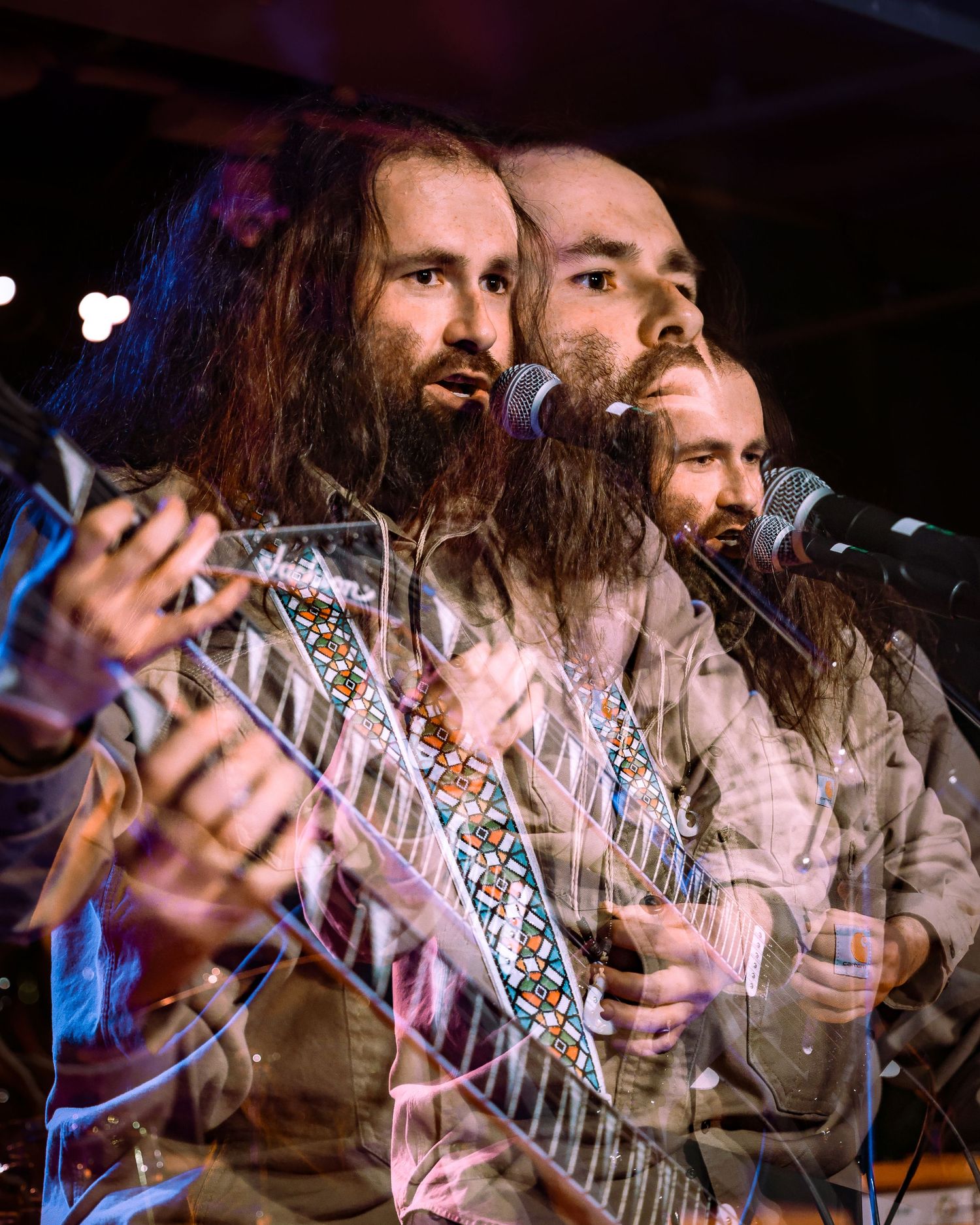 Multiple exposure photo of a long-haired bearded guitarist singing at a microphone on stage.