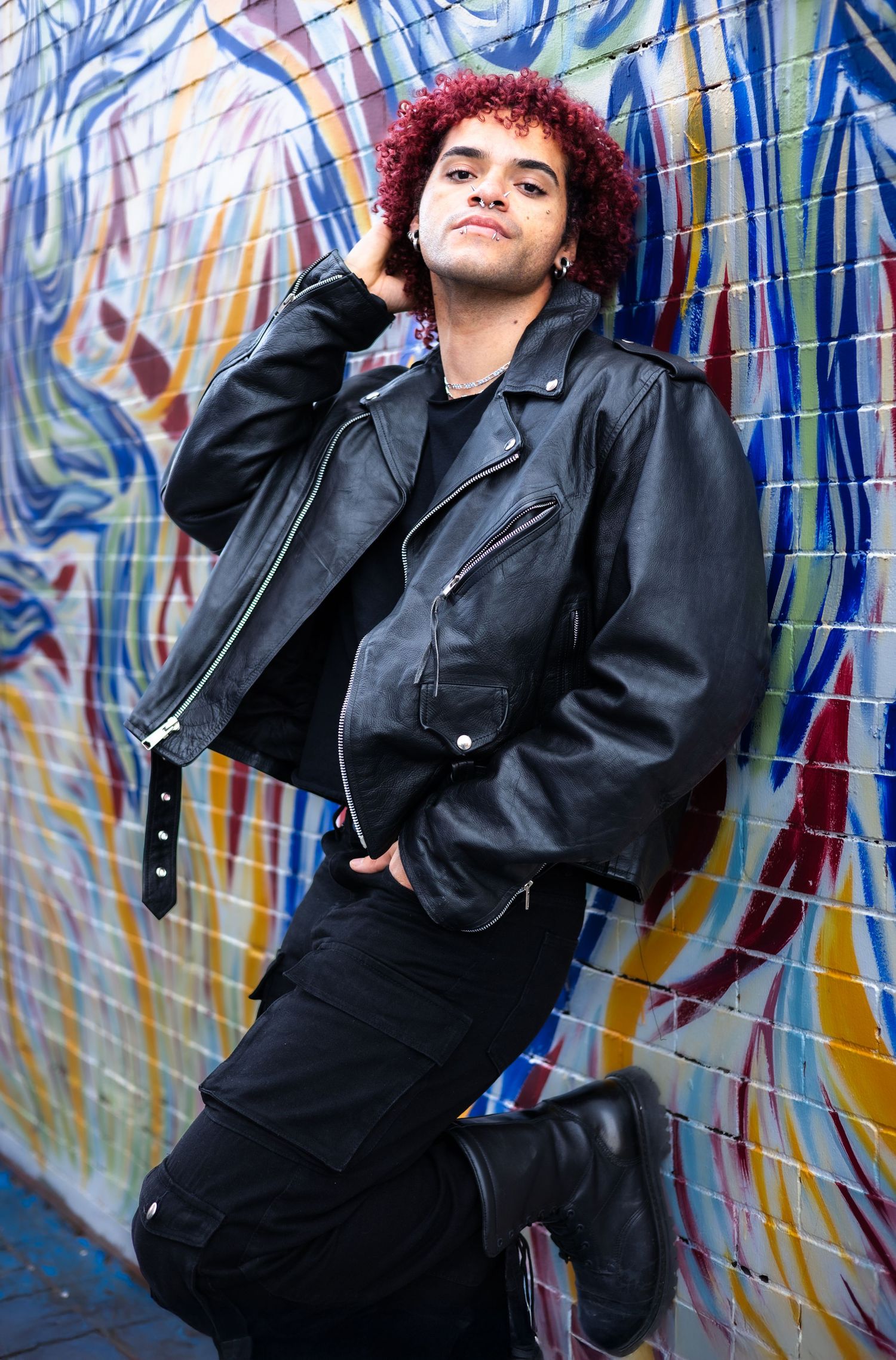 Figure in dark outfit poses dramatically against graffiti backdrop.