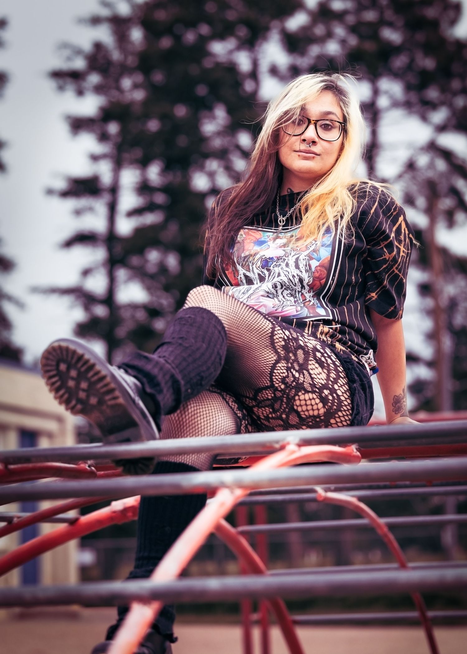 Alternative style portrait of someone in glasses and boots sitting on playground equipment.