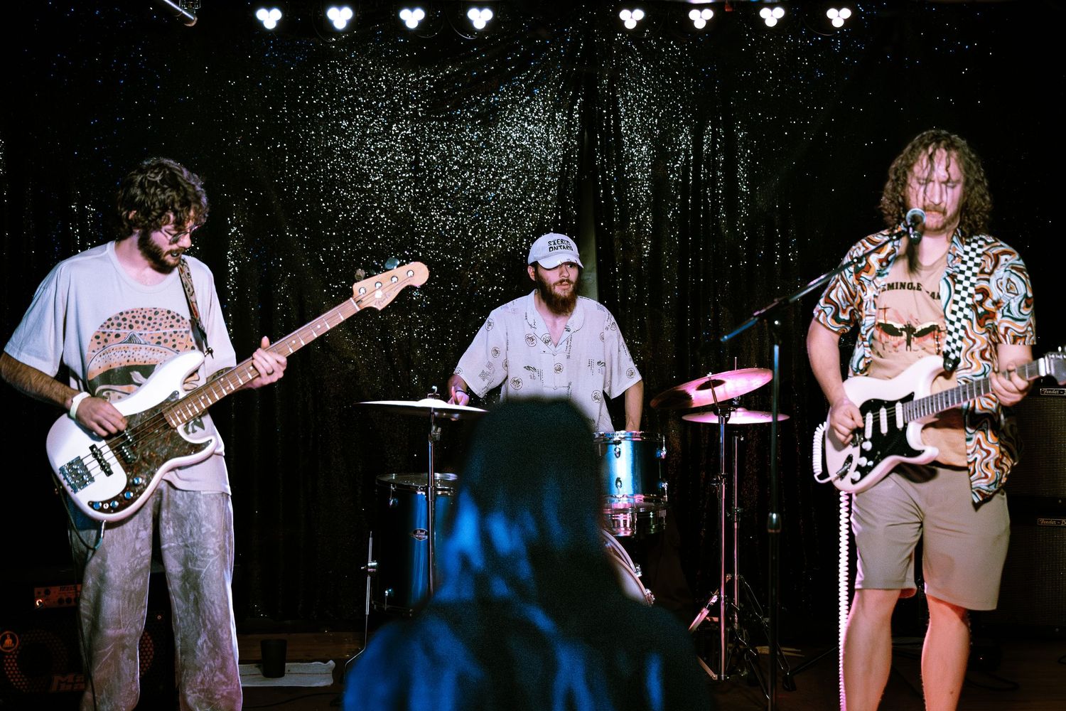 Three-piece rock band performing live on stage with guitarist, drummer, and bassist in a dark venue.