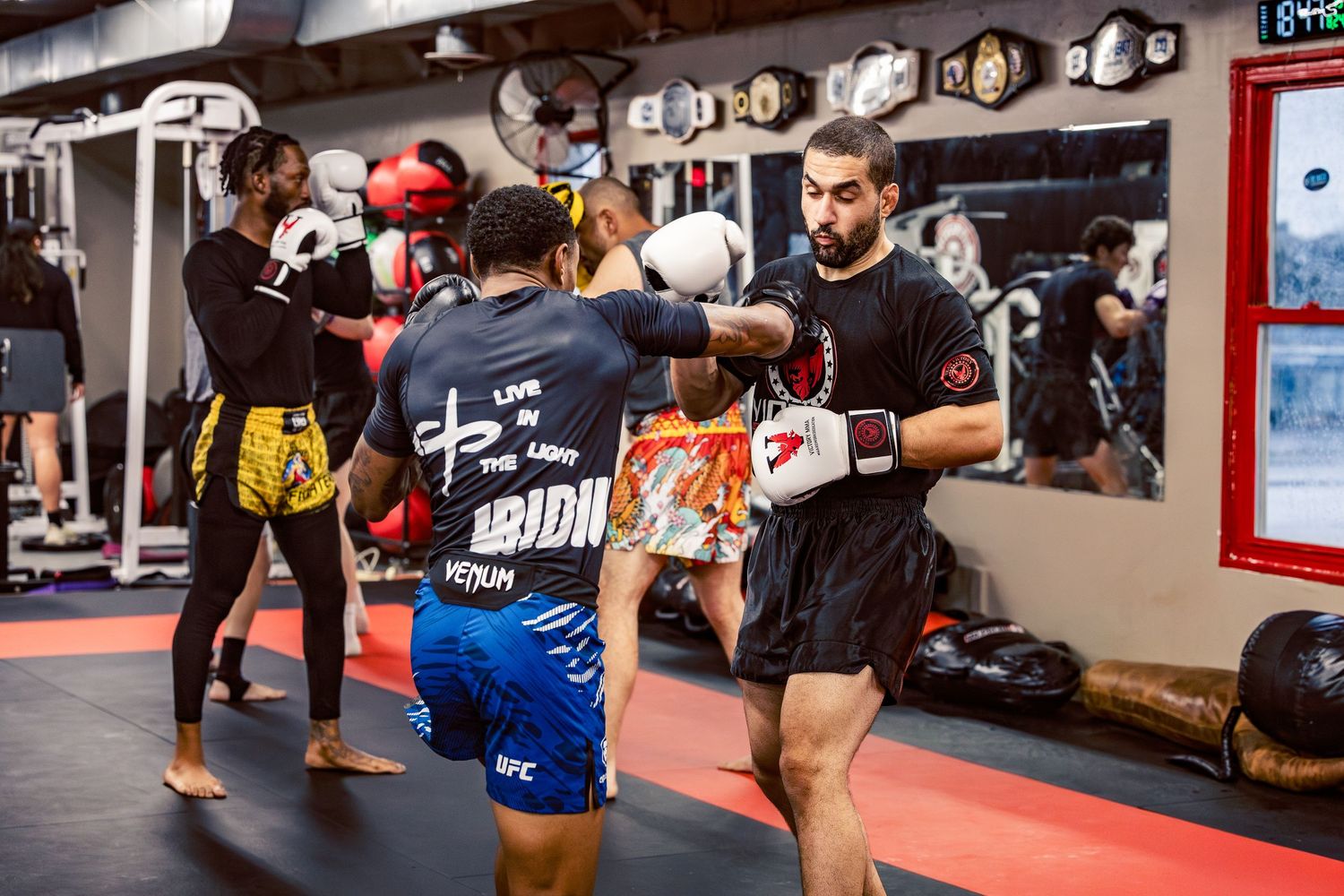 Combat sports practitioners sparring and practicing kicks in a well-equipped martial arts facility.