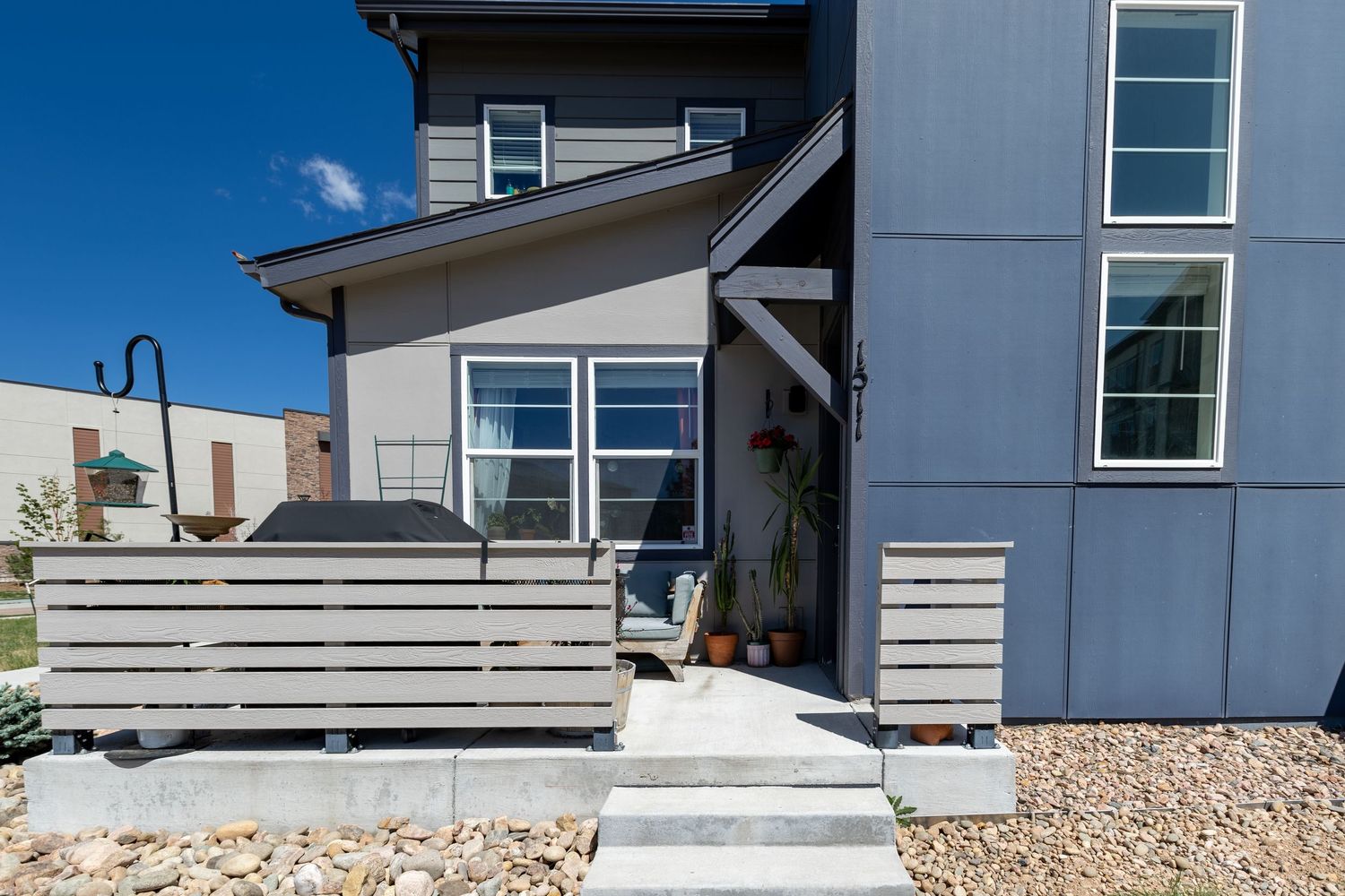 Modern gray home exterior featuring horizontal wood fence, concrete steps, and large windows under a clear blue sky.