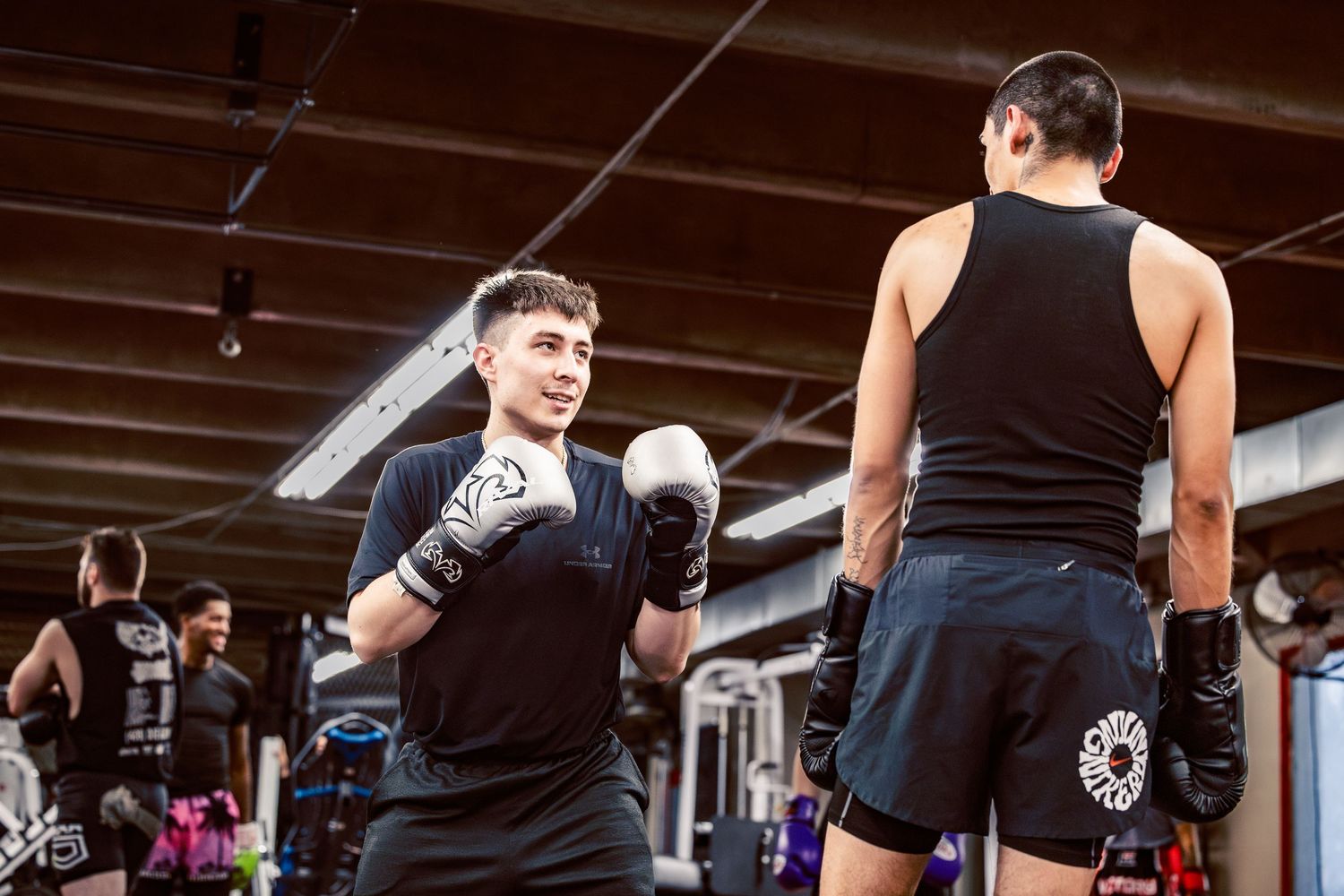 Fighters training with boxing gloves in a dimly lit combat sports facility.