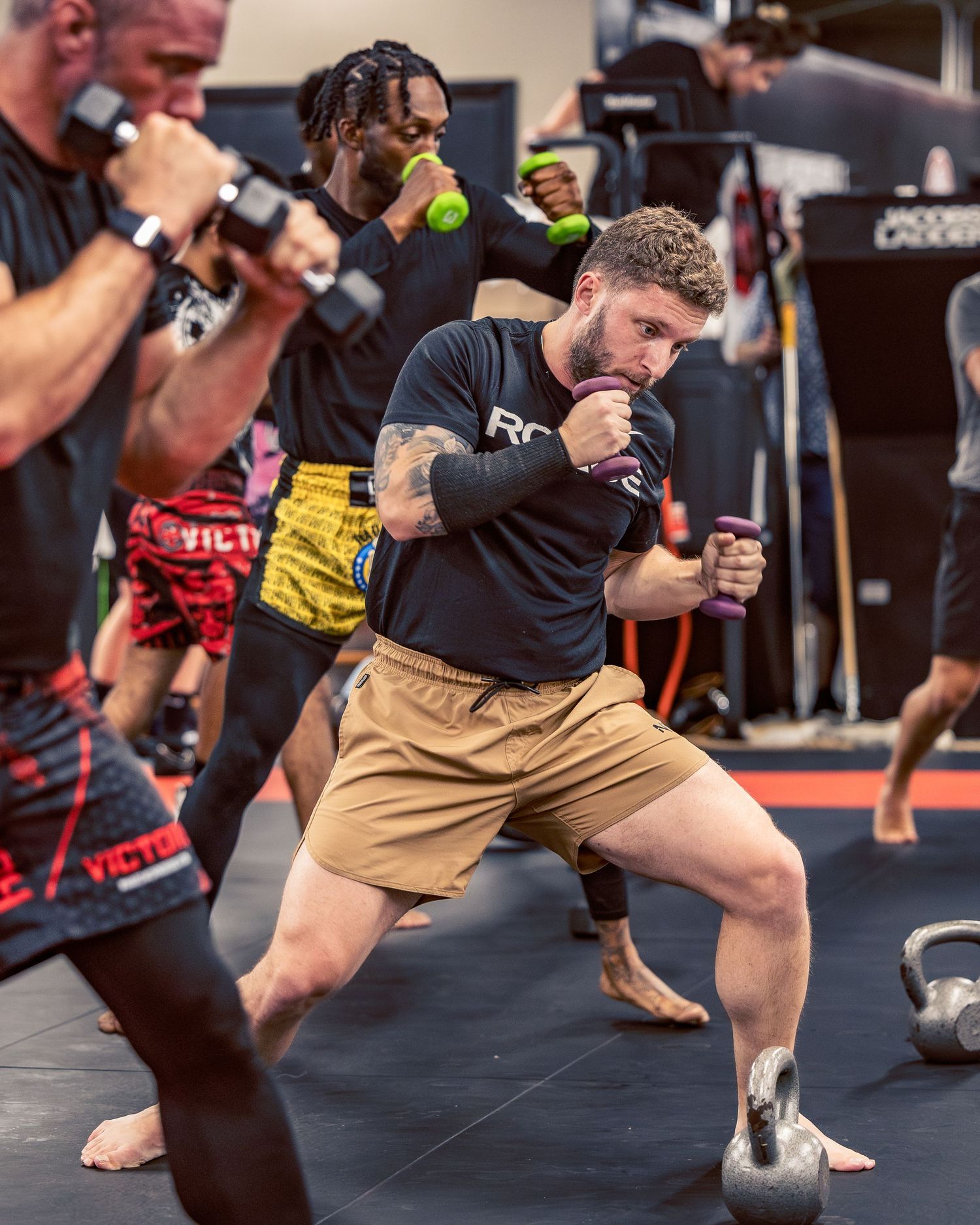 Athletes performing dynamic striking drills with training equipment in a martial arts facility.