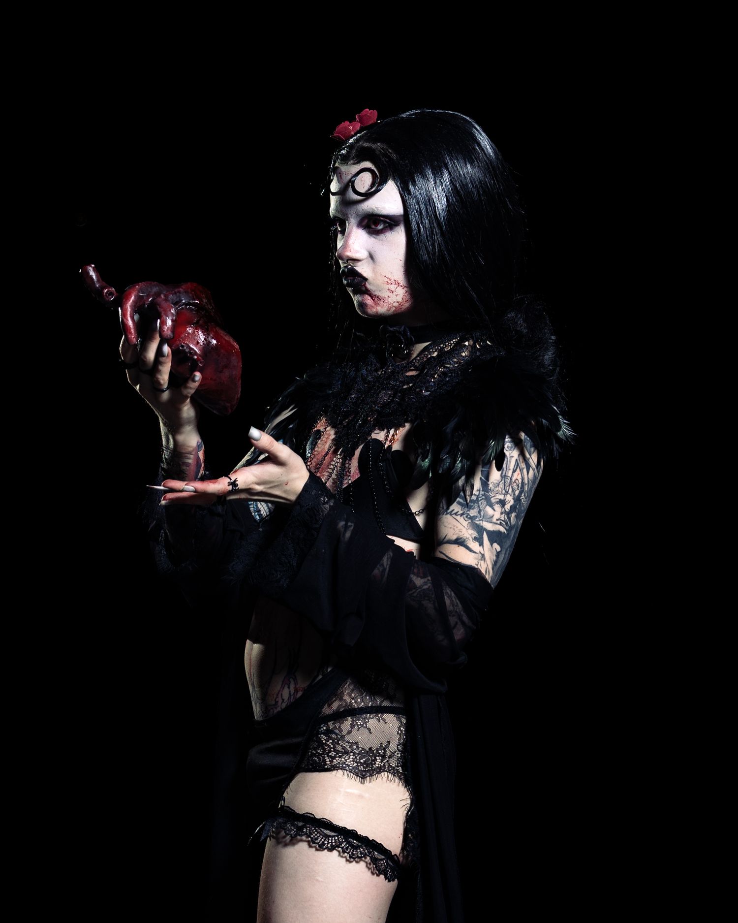 Gothic woman in black lace holding a bloody heart prop, dark fantasy Halloween costume with dramatic makeup.