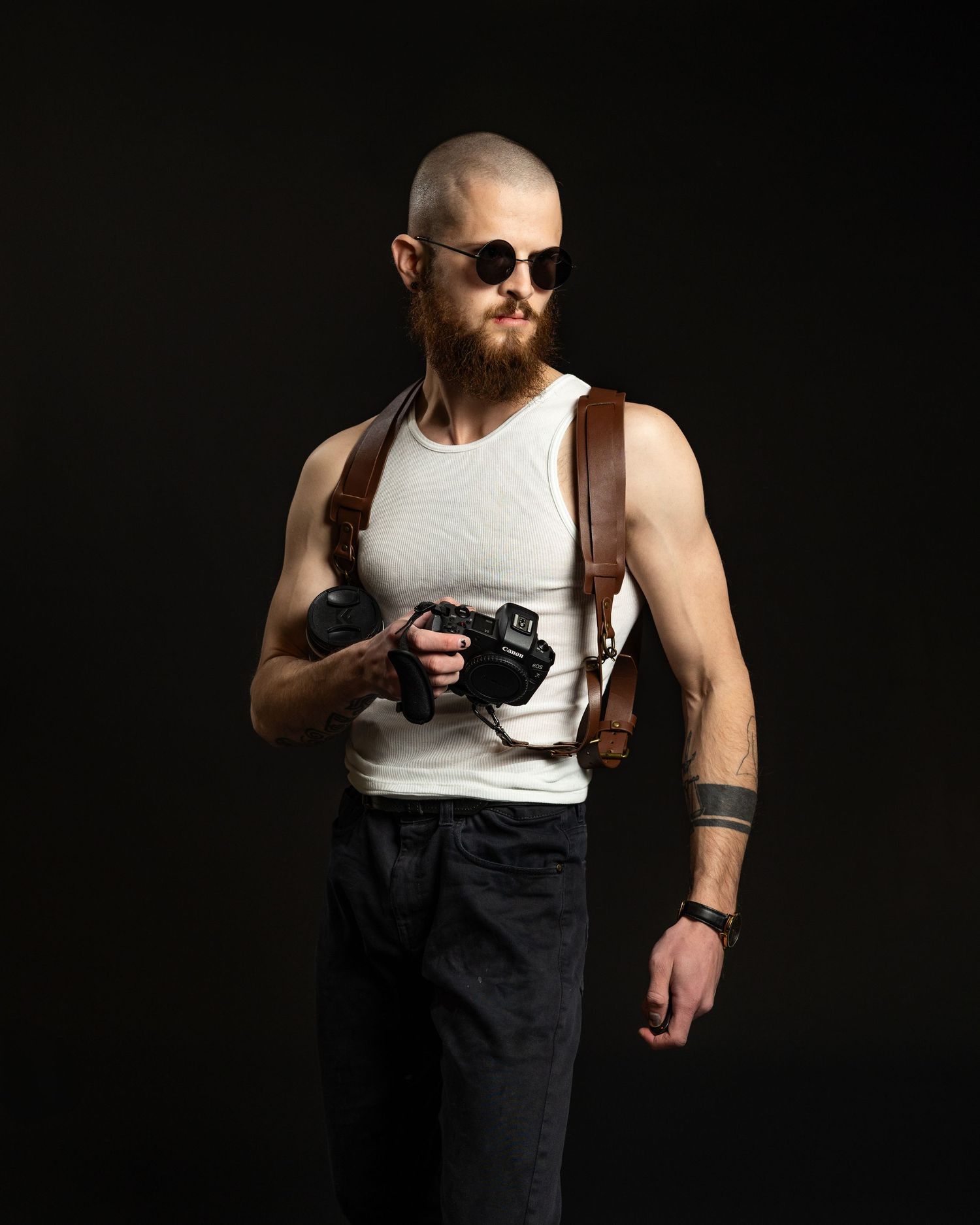Dramatic studio portrait of a muscular person in a white tank top and dark pants against a black background.