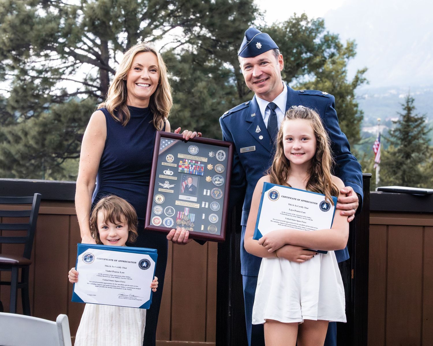 Family members displaying military awards and certificates during outdoor ceremony.