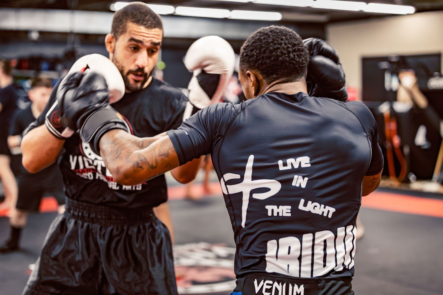 Athletes wearing protective gear while training boxing combinations in an indoor facility.