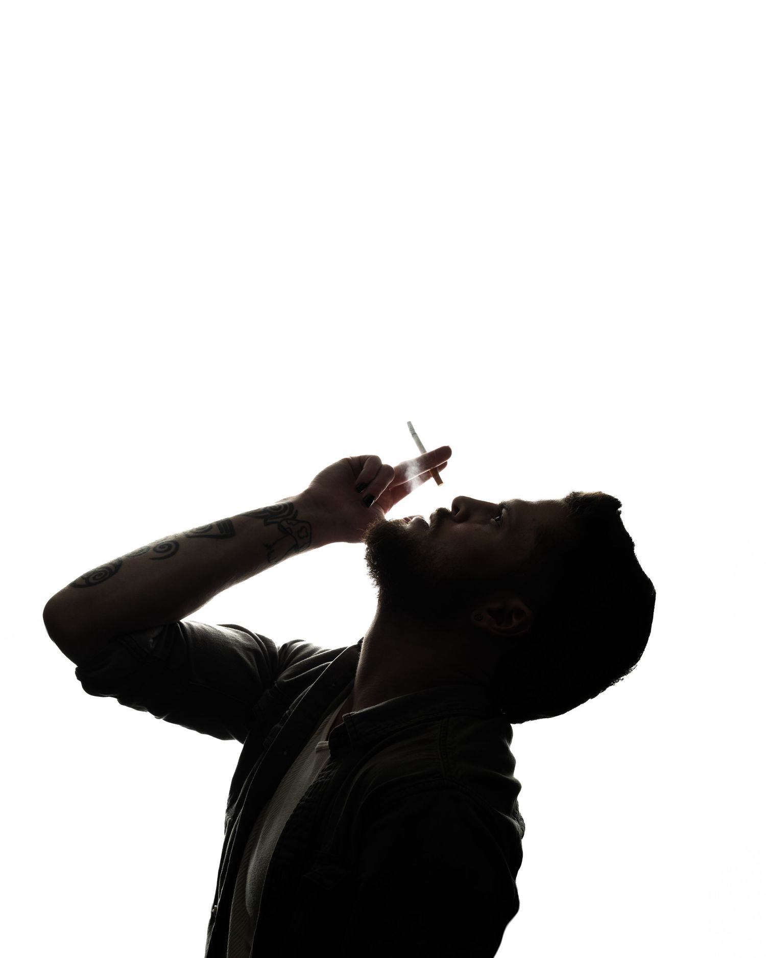 Silhouette of a man tilting his head back holding a cigarette against a white background.