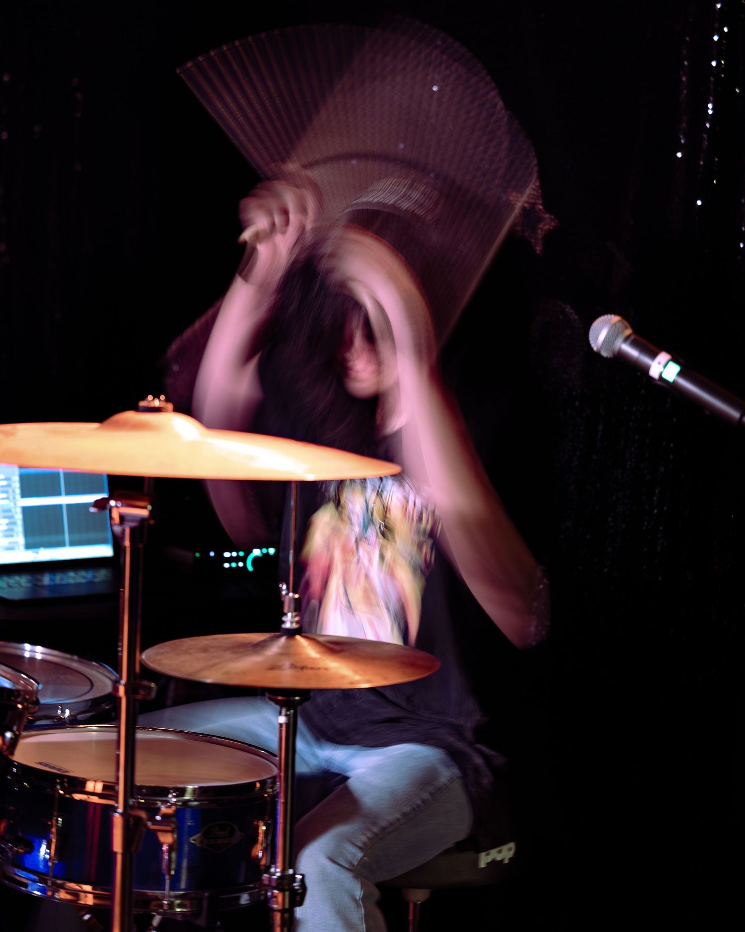 Dynamic motion blur shot of drummer performing energetically on stage.