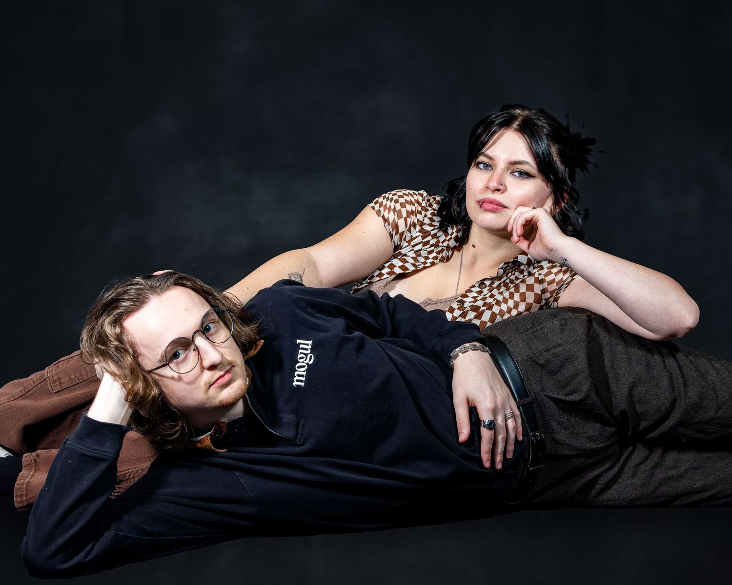 Man and woman posing together in elegant studio portrait against dark backdrop.