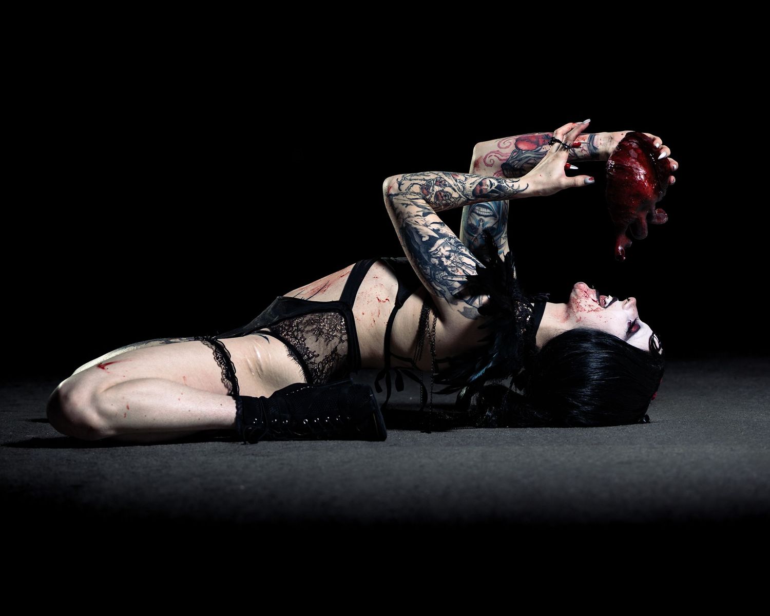Tattooed woman in black lingerie posing dramatically on dark floor with red hair cascading down.