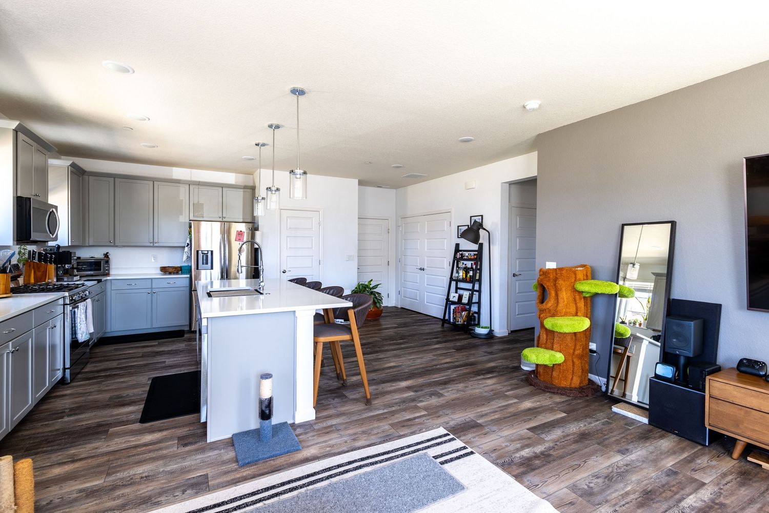 Modern open-concept kitchen with gray cabinets, white island, hardwood floors, and pendant lighting.