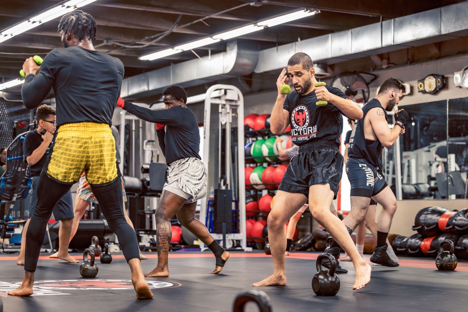 Panoramic view of a group fitness class doing lunges on red mats in a gym setting.