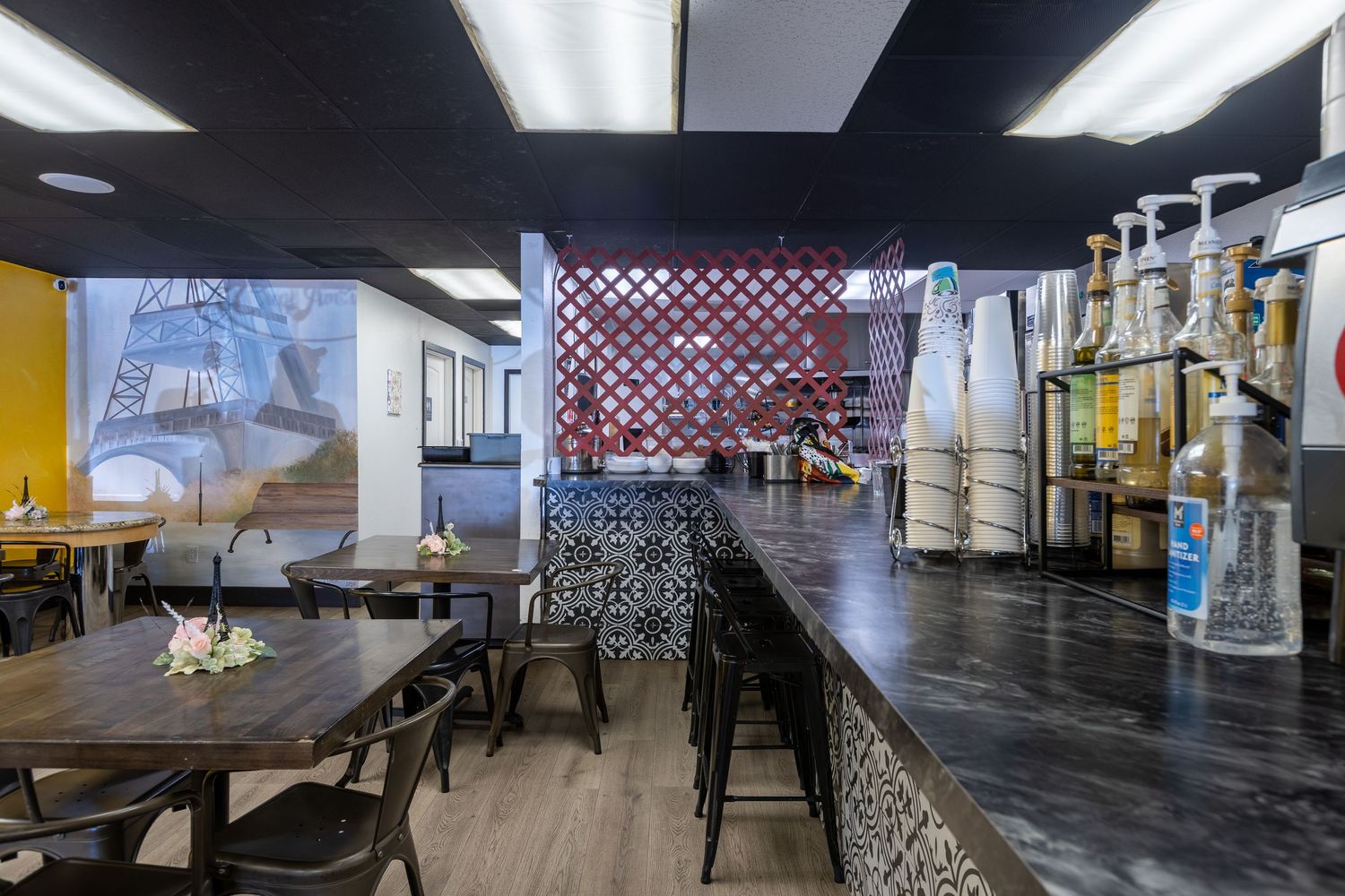 Modern restaurant interior with dark bar counter, hookah pipes, lattice divider, and Eiffel Tower mural on the wall.
