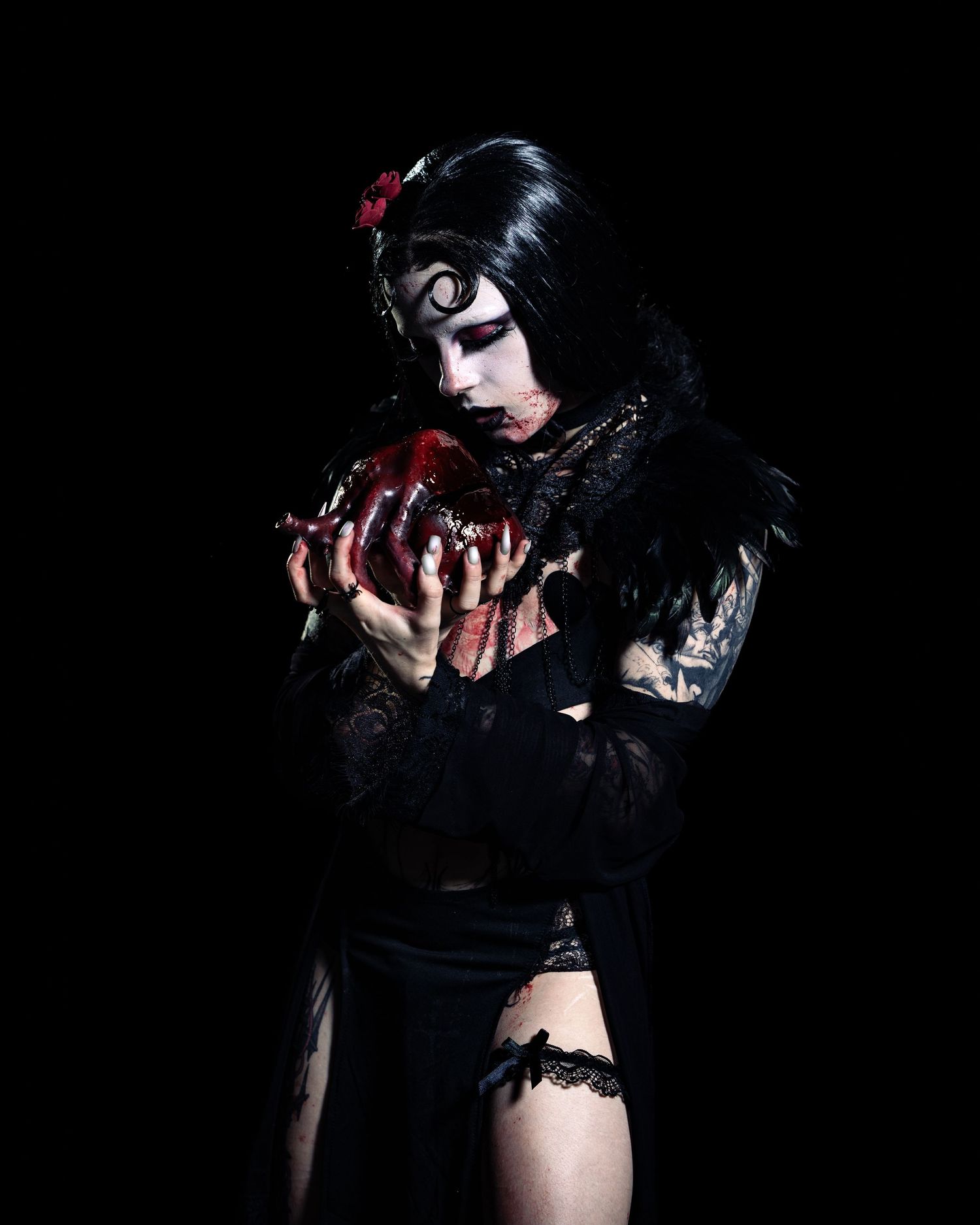 Gothic woman in black lace dress holding bloody heart, dramatic dark makeup and feathers, Halloween costume art.