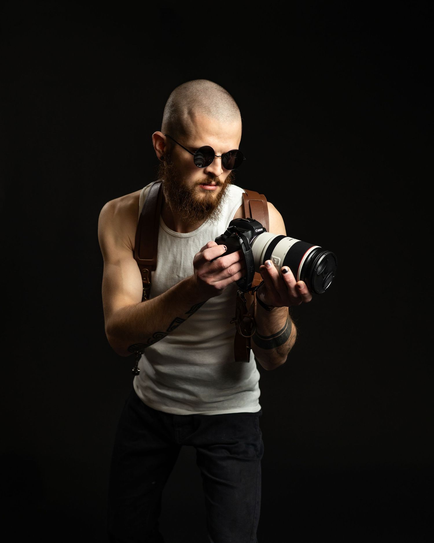 Photographer in white tank top adjusts camera settings while shooting in dramatic lighting.