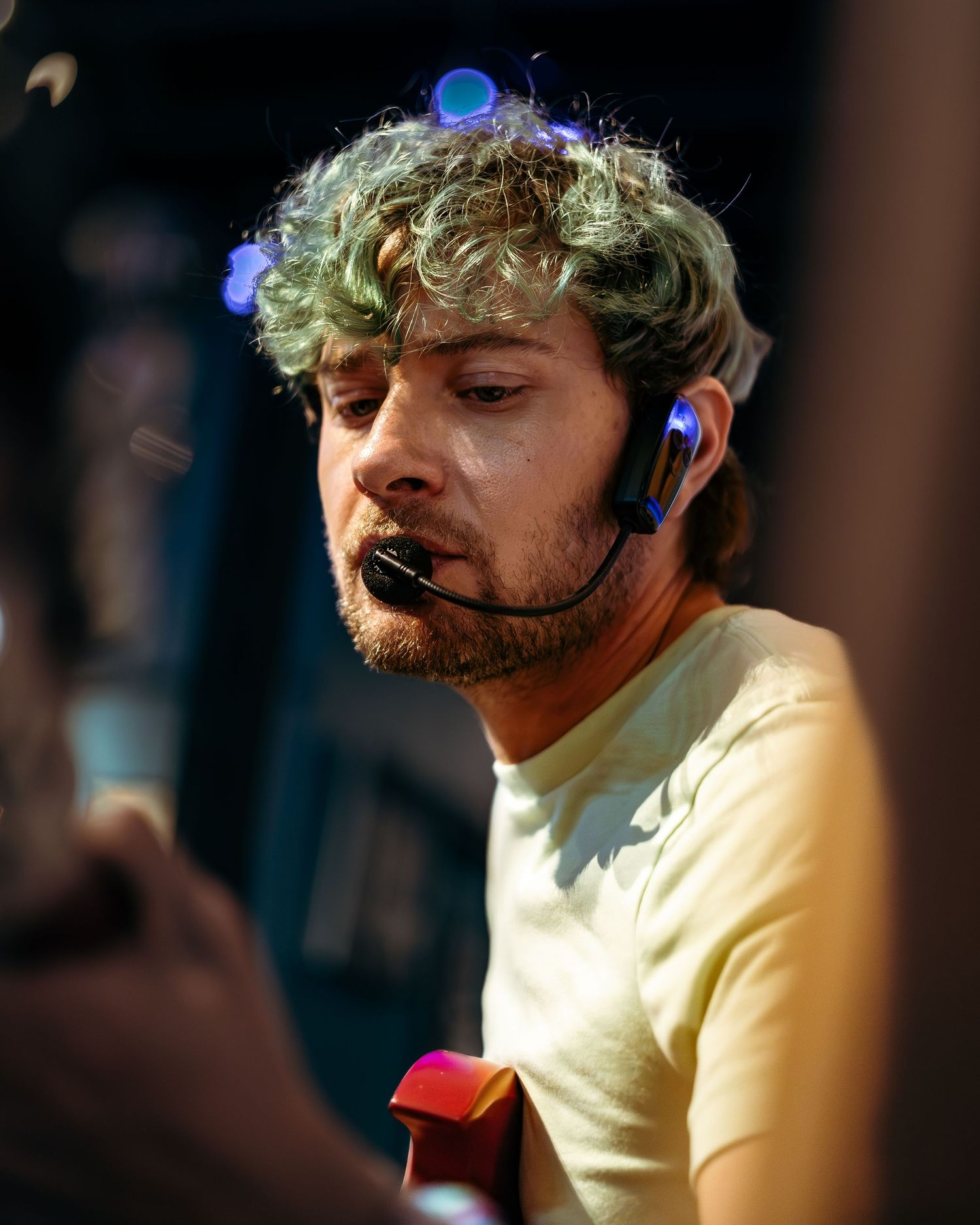 A performer in a yellow shirt sings passionately into a microphone during a live performance in dramatic lighting.
