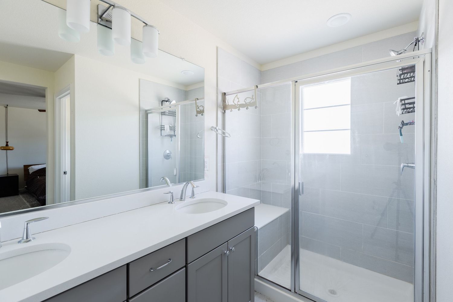 Elegant bathroom with gray vanity, white quartz countertop, large mirror, and glass-enclosed shower.