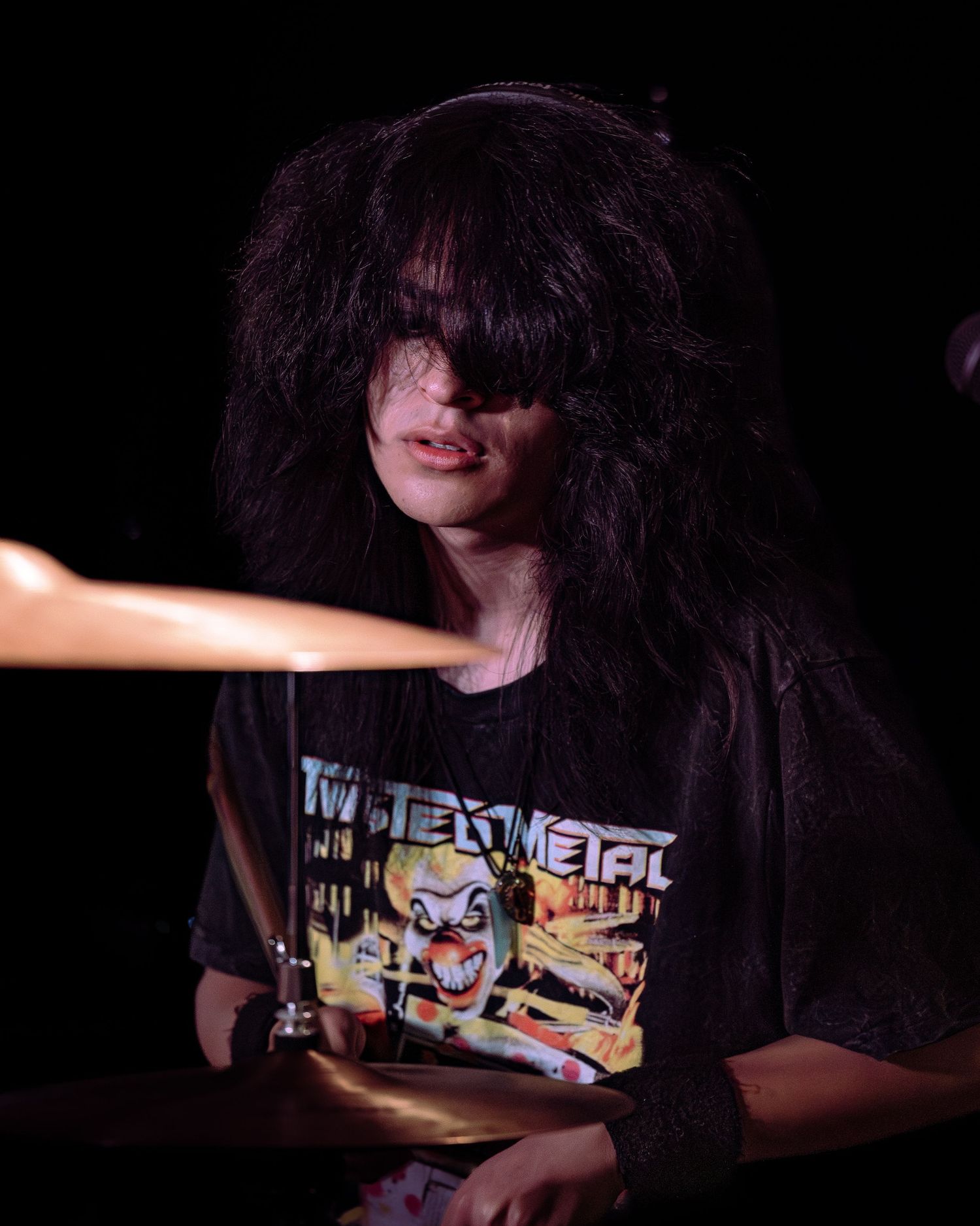 Young drummer with long black hair playing drums in dark concert venue.