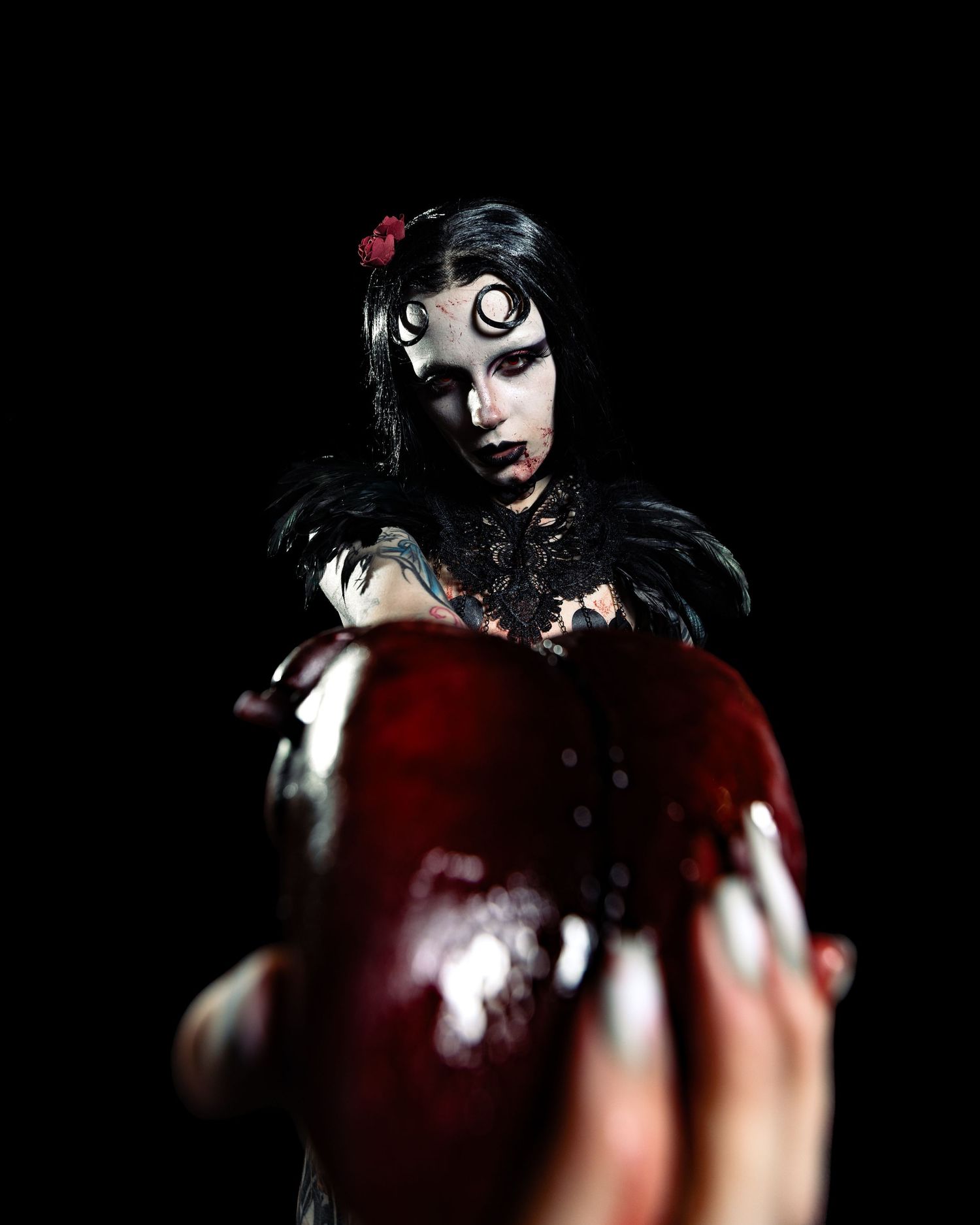 Gothic Snow White cosplay with dramatic skull makeup, black feather costume, holding a glossy red poison apple in dark setting.