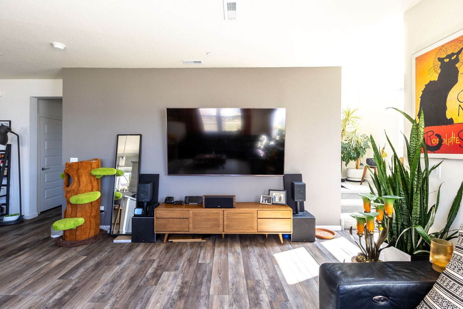 Modern living room with wall-mounted TV, mid-century media console, hardwood floors, and lush indoor plants.