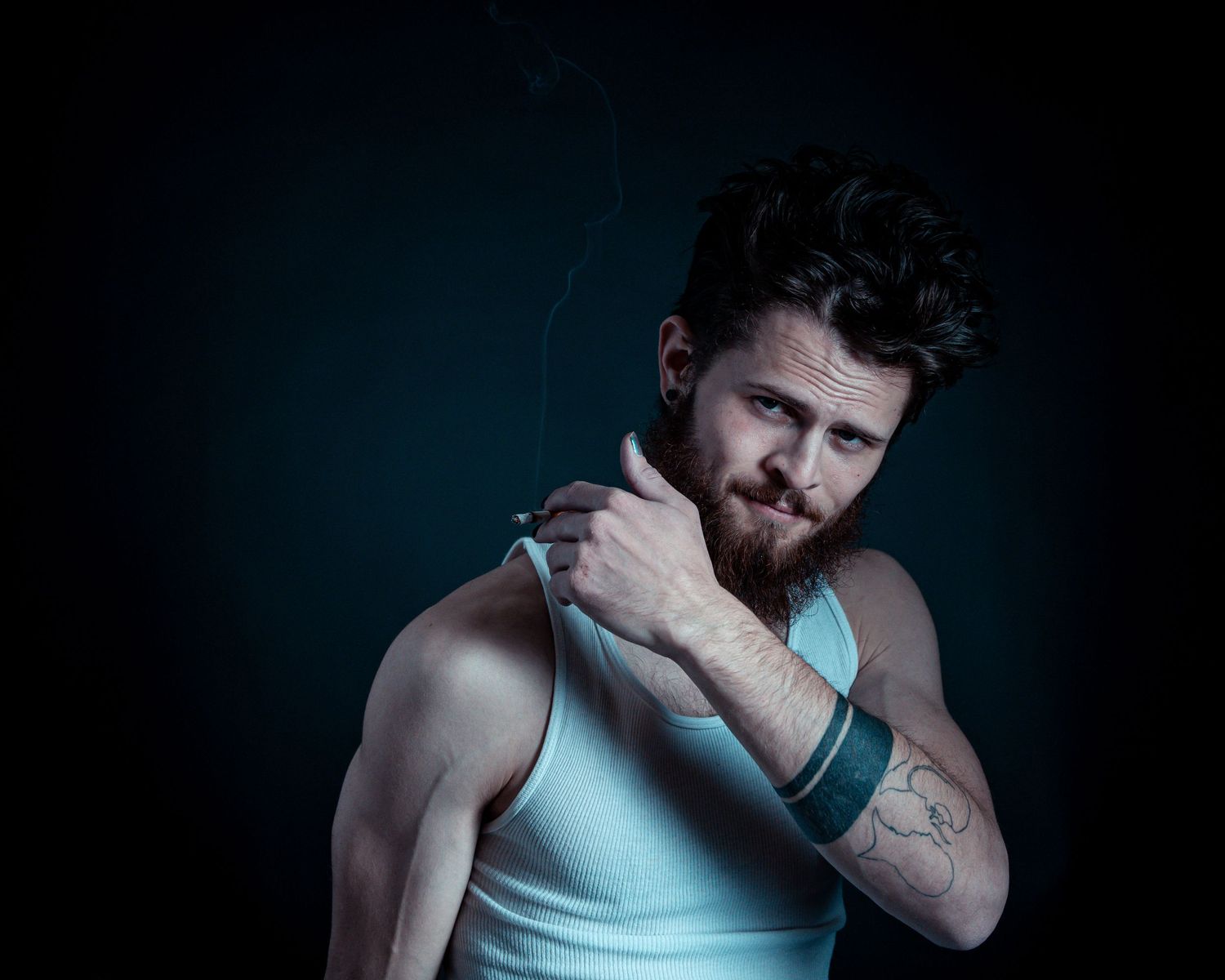 Dramatic studio portrait of muscular person in tank top with tattoo against dark background.