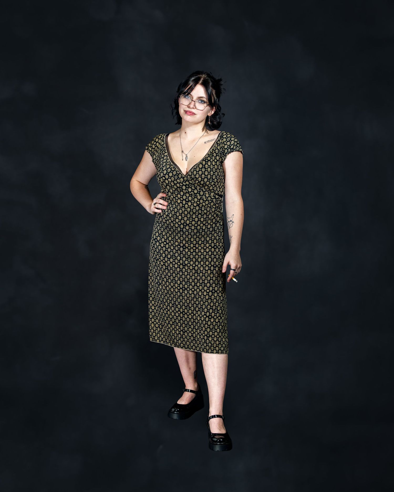 Woman in green polka dot midi dress posing confidently against dark studio backdrop.