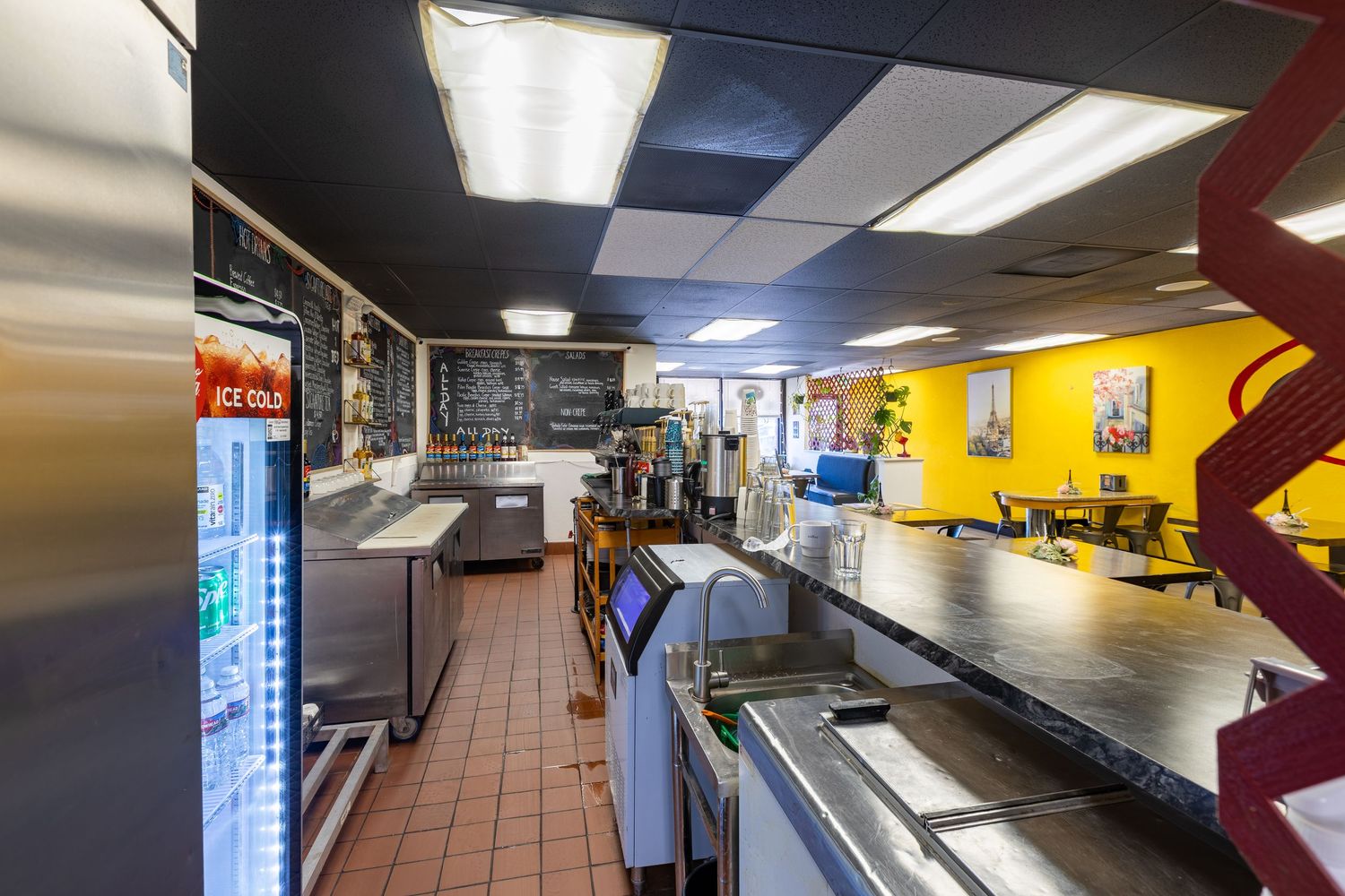 Interior view of a commercial restaurant kitchen and serving counter with yellow walls and refrigerated display cases.