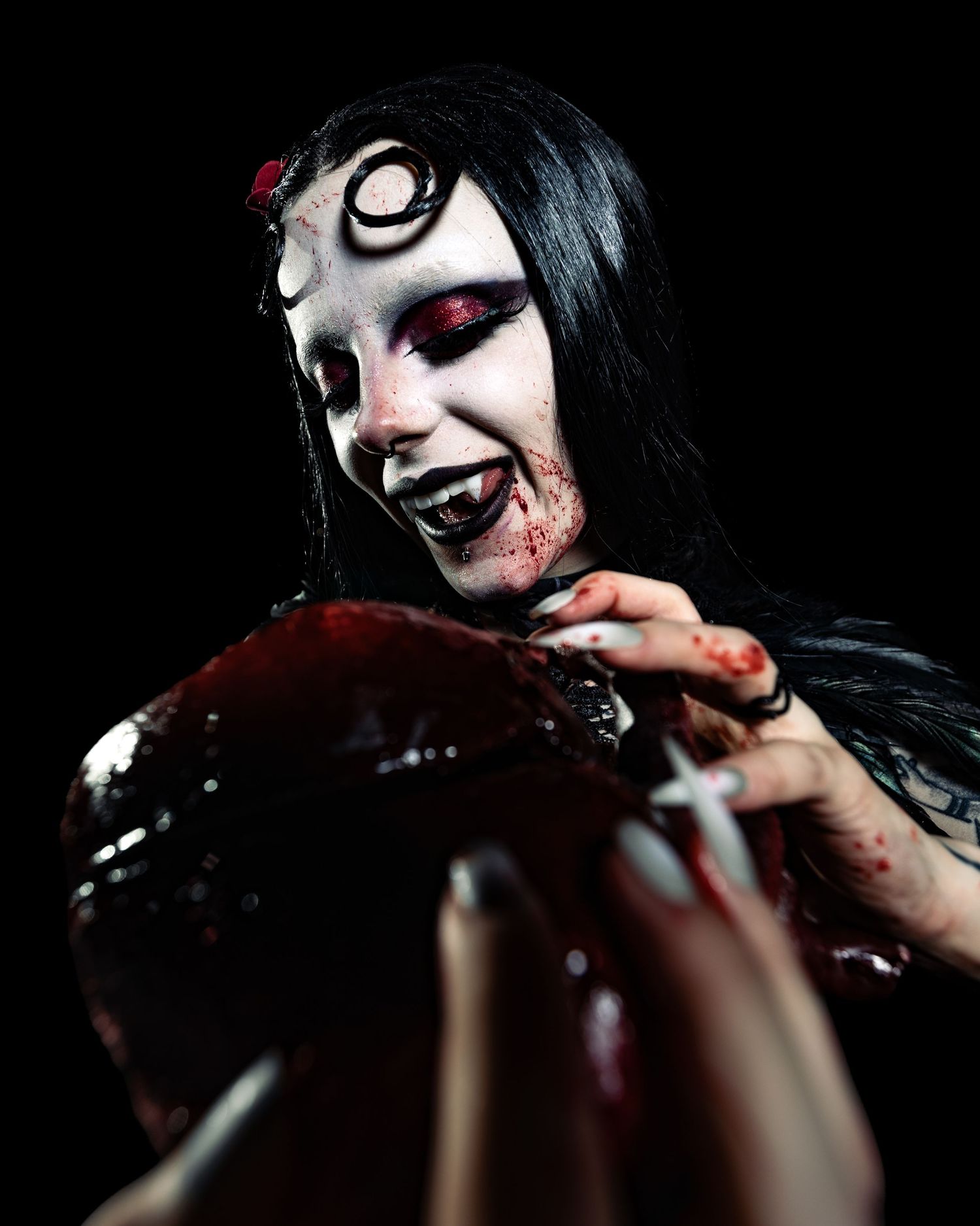 Gothic performer with spiral eye makeup and bloody horror costume holds a dark prop on black background.