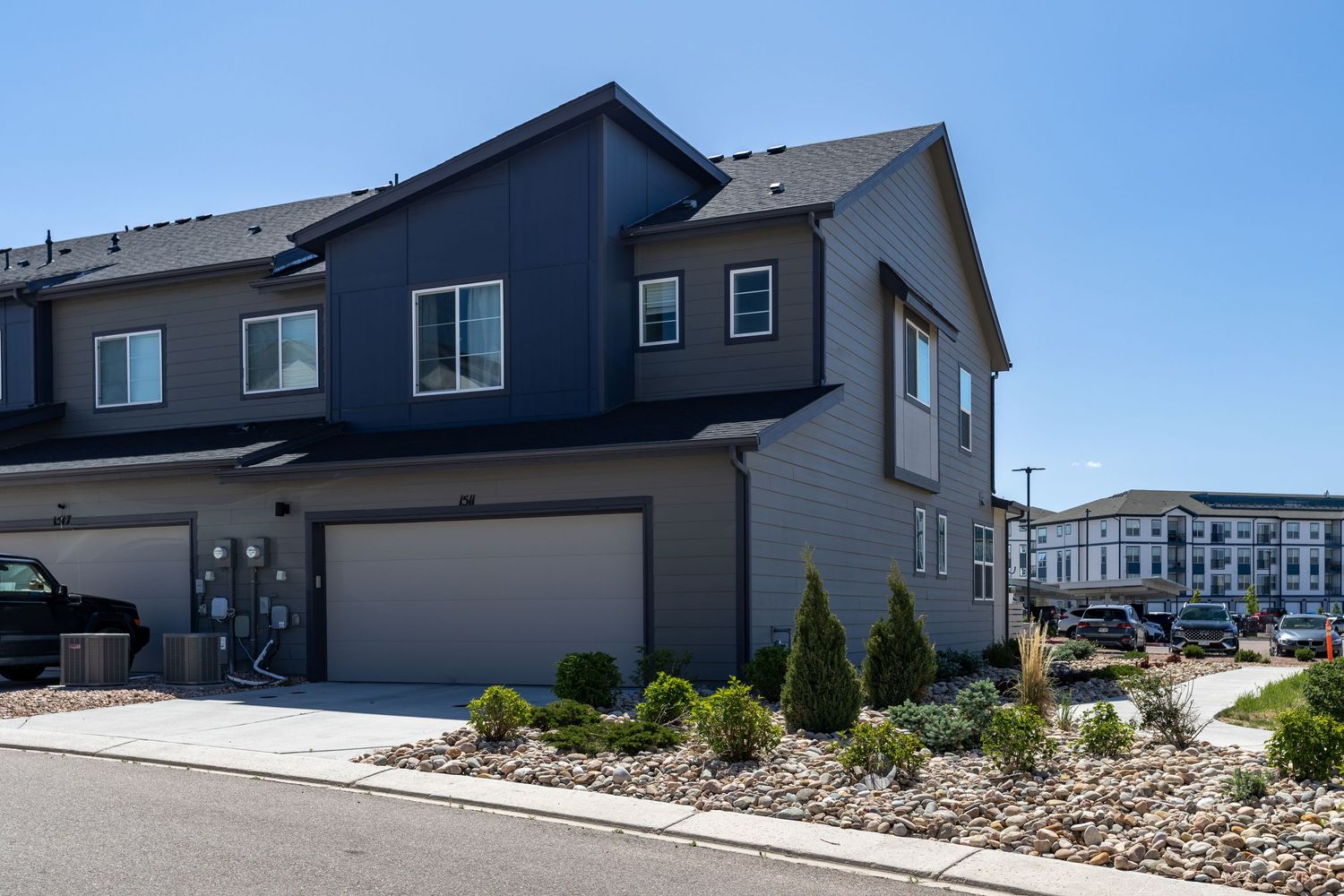 Modern two-story townhome with gray siding, two-car garage, and landscaped front yard under a clear blue sky.