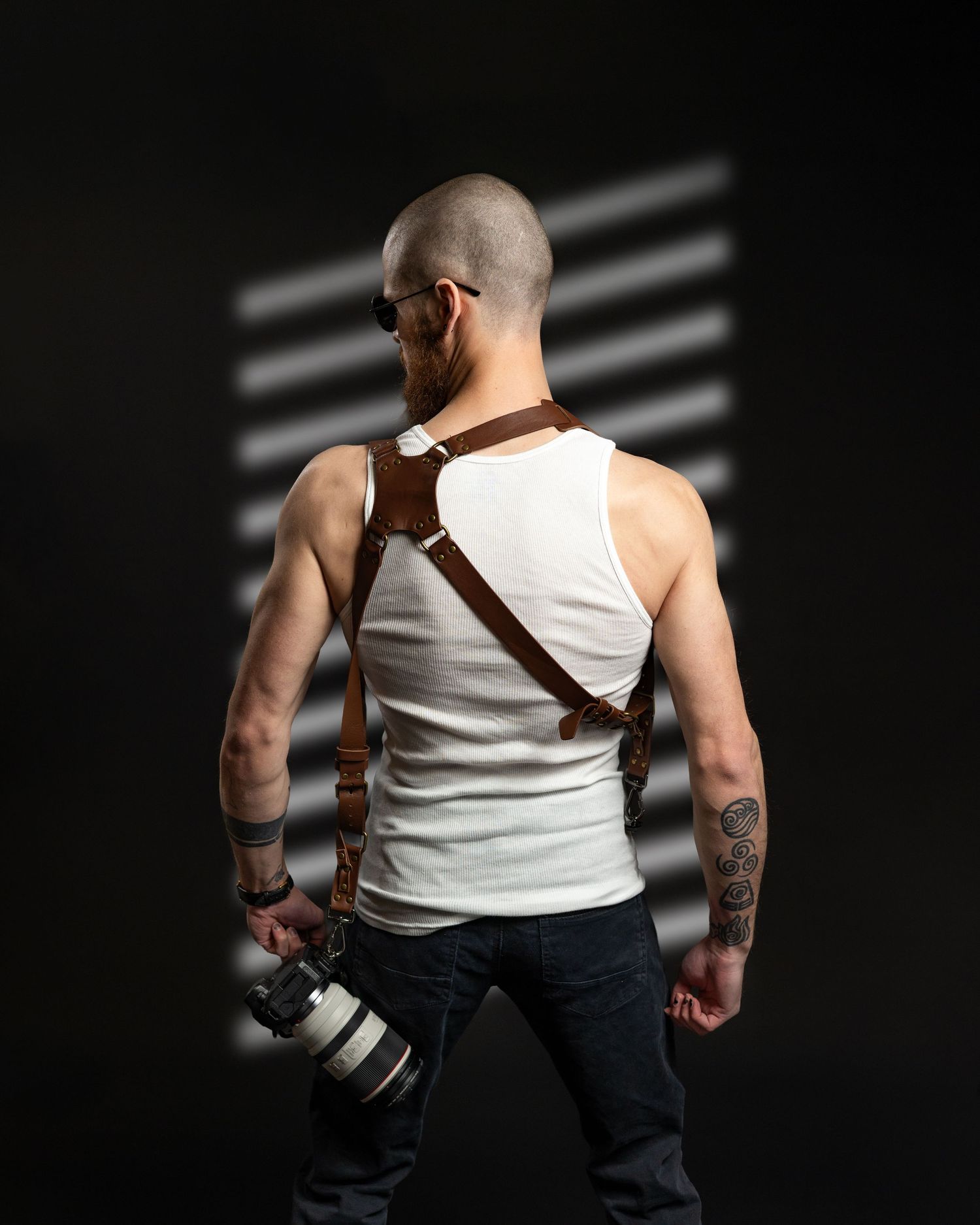 Back view of photographer wearing white tank top with camera strap across shoulder in studio.