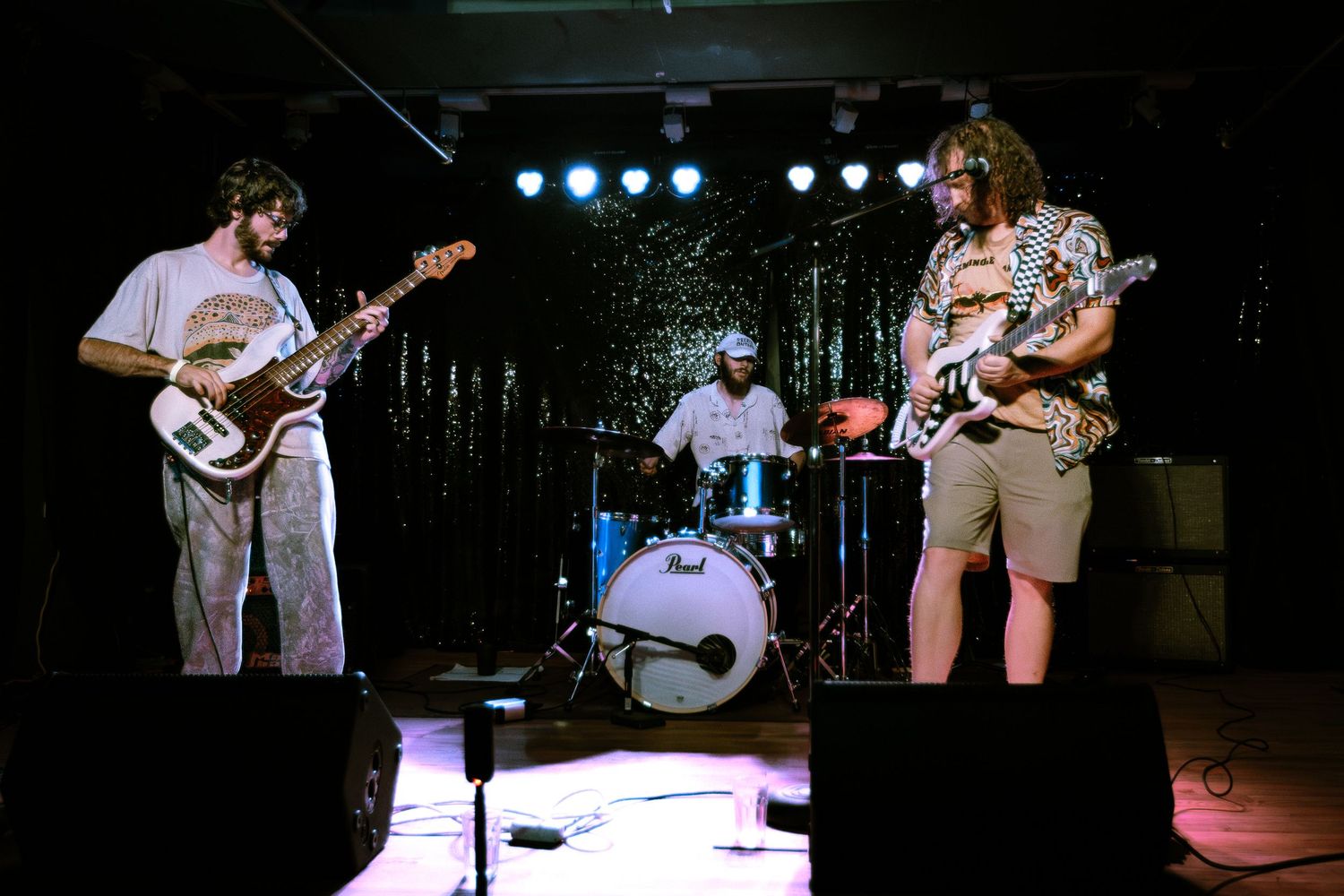 Three-piece rock band performing on stage with Pearl drum kit in venue.