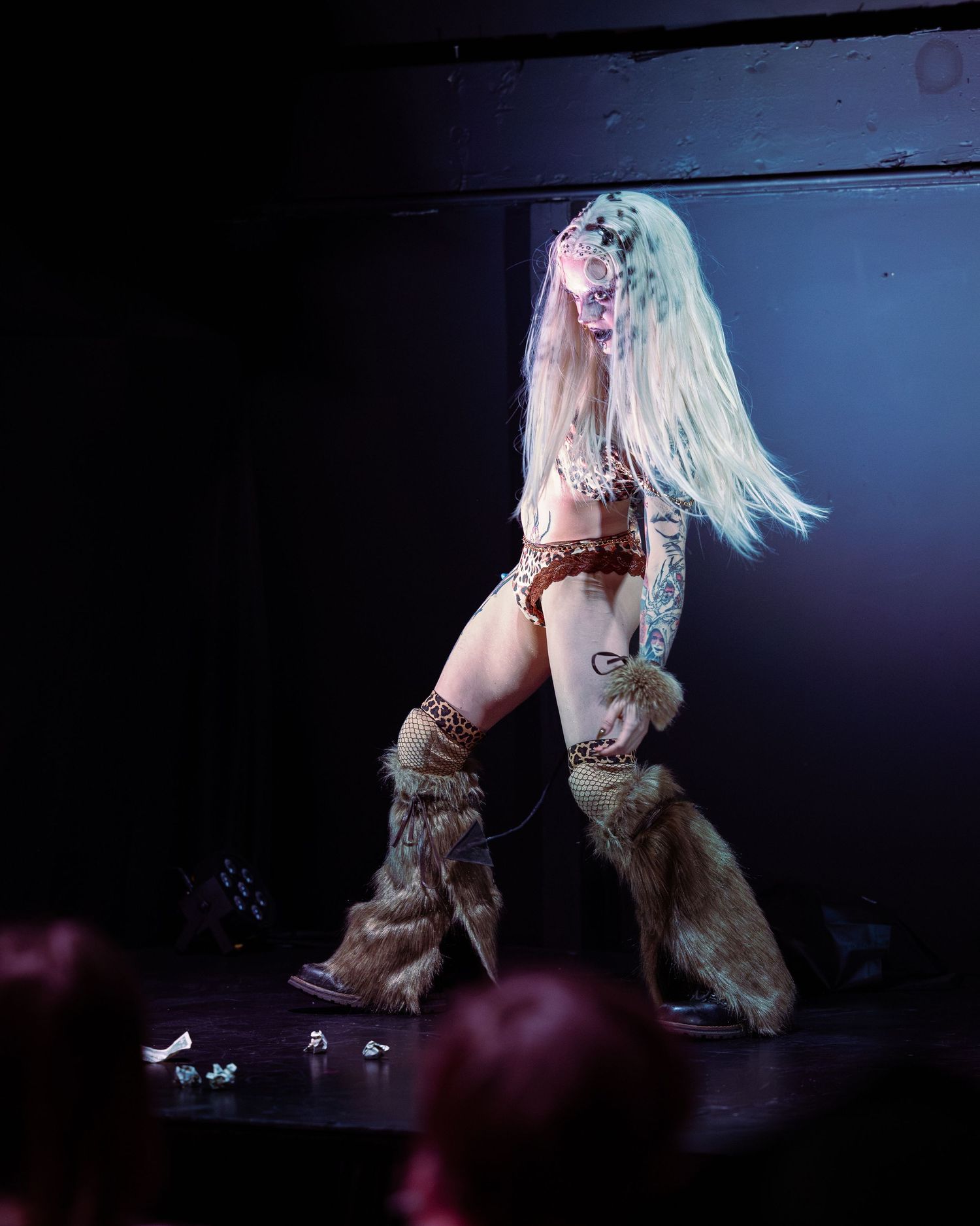 Tattooed performer in leopard print and fur boots tossing long blonde hair on stage.