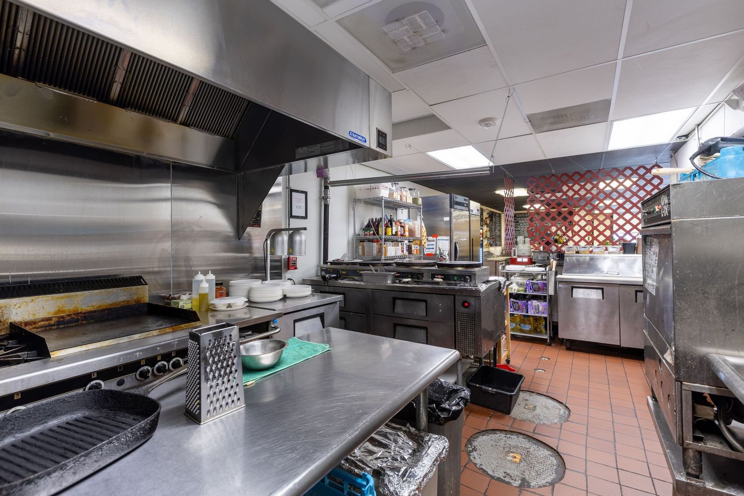 Stainless steel commercial kitchen with professional cooking equipment, prep surfaces, and ventilation hood in a restaurant.