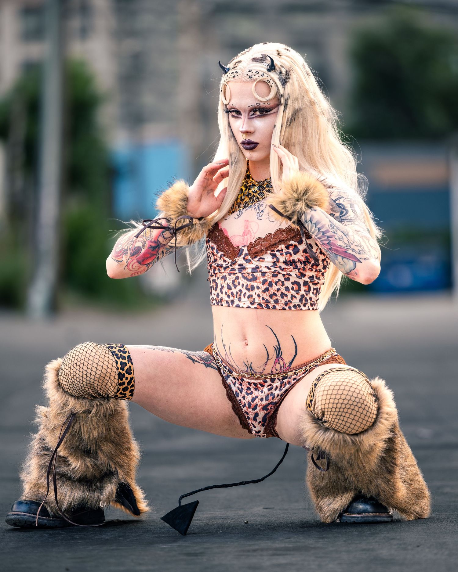 Tattooed performer in leopard print costume with fur boots and horned headpiece posing dramatically outdoors.