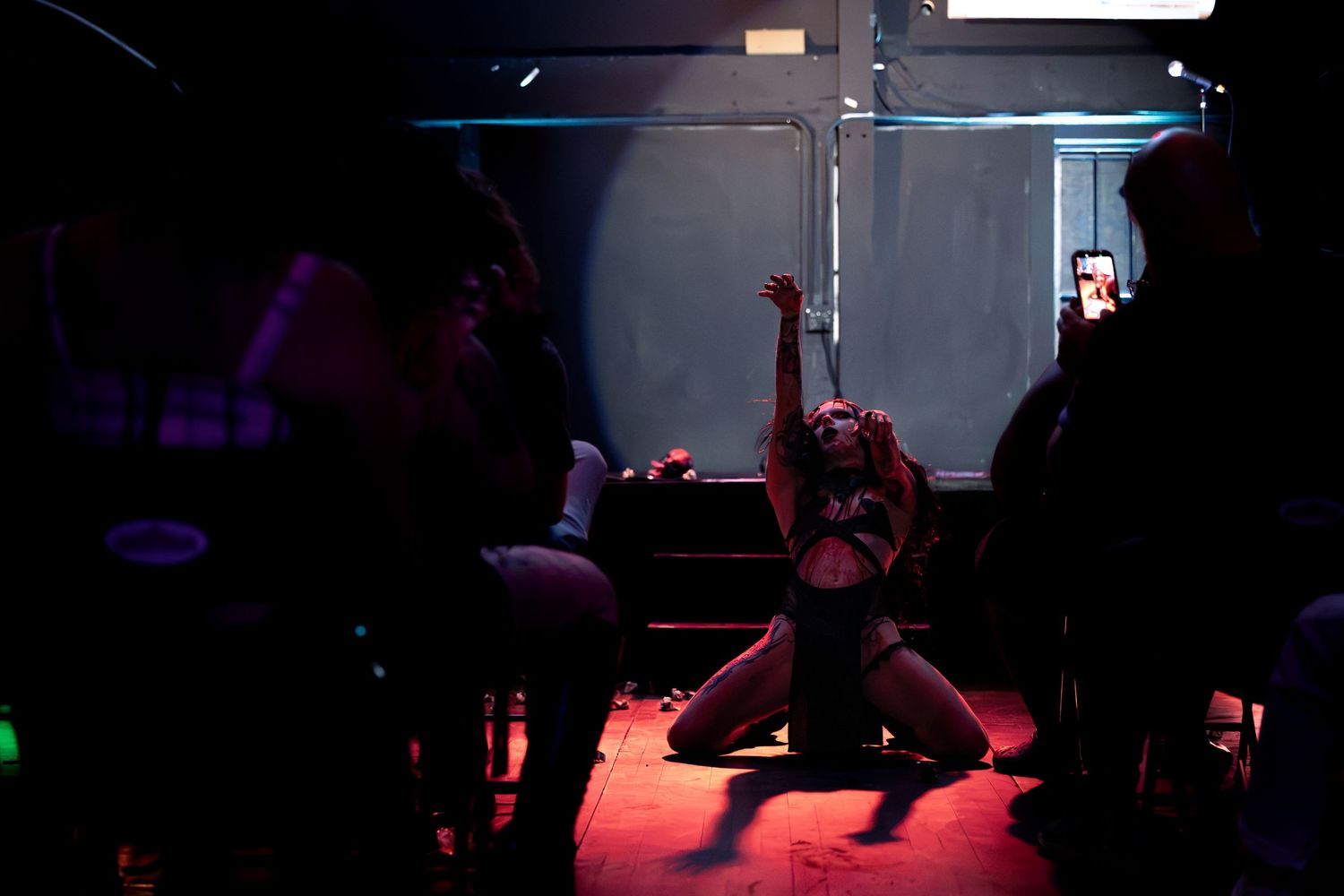 A performer dances on stage in dramatic red lighting at a dark nightclub venue.