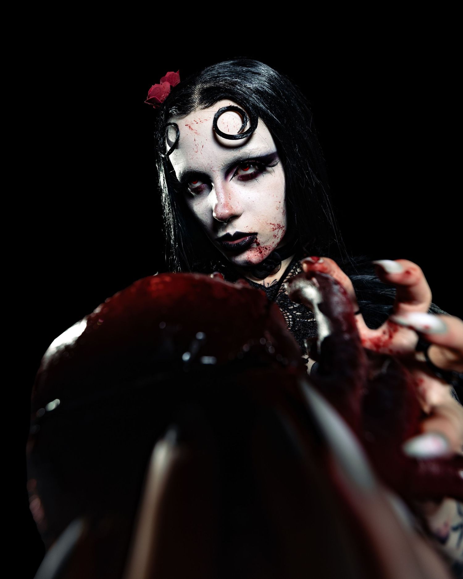 Gothic vampire costume performer with spiral eye makeup and blood effects poses dramatically in dark setting.