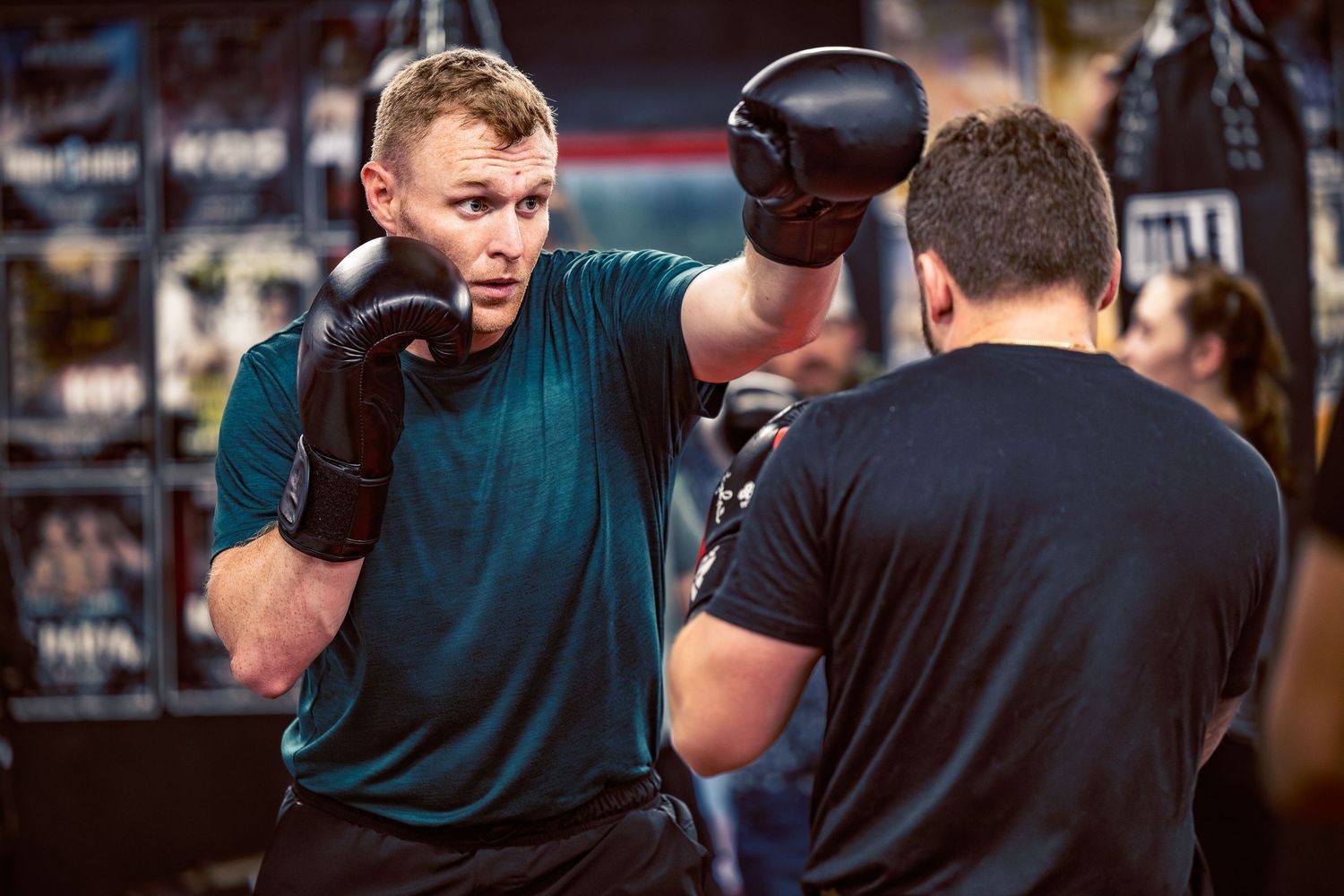 Boxers engage in sparring practice while wearing black and teal athletic gear.
