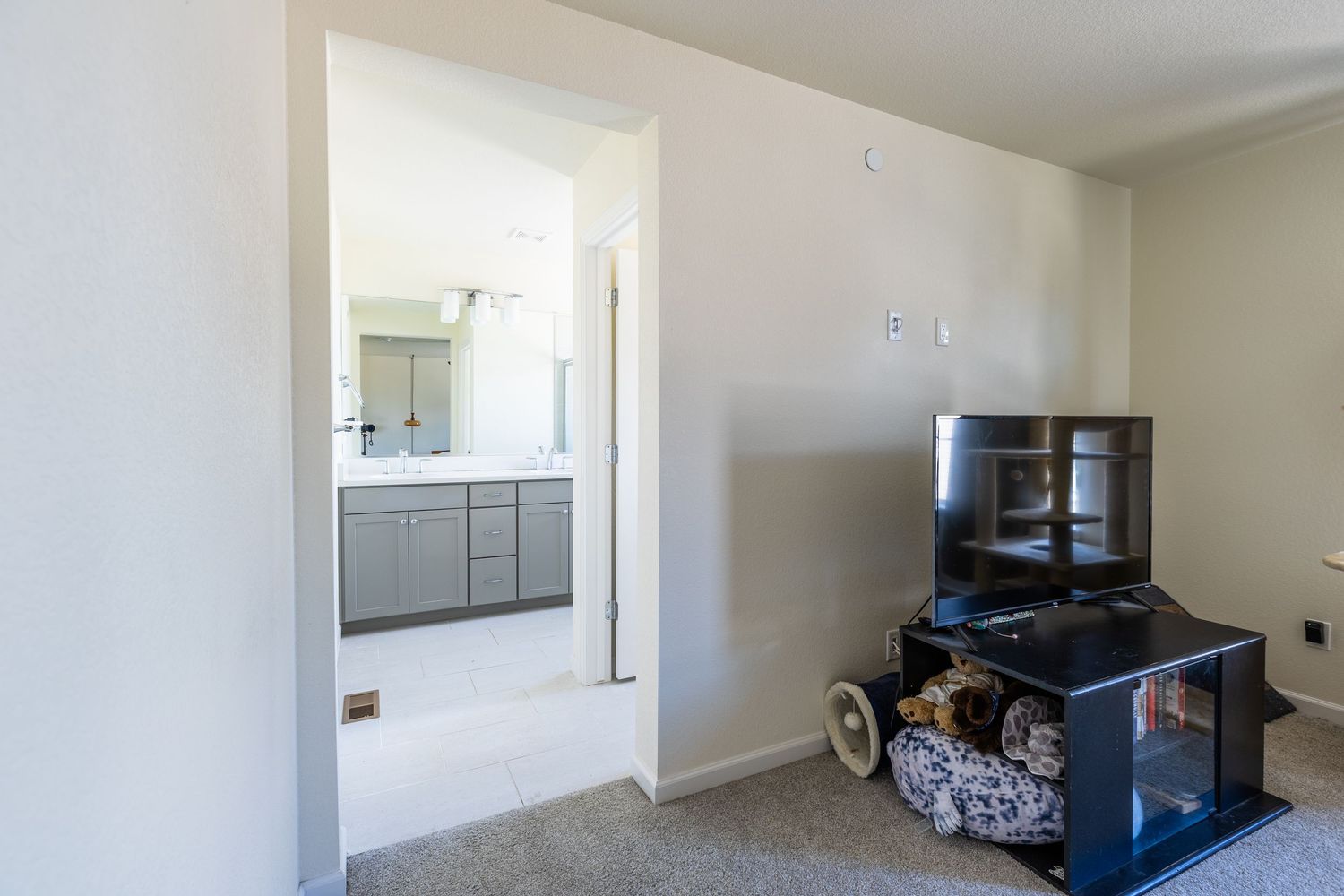 Bedroom with carpet flooring and open doorway leading to a modern bathroom with gray vanity and large mirror.