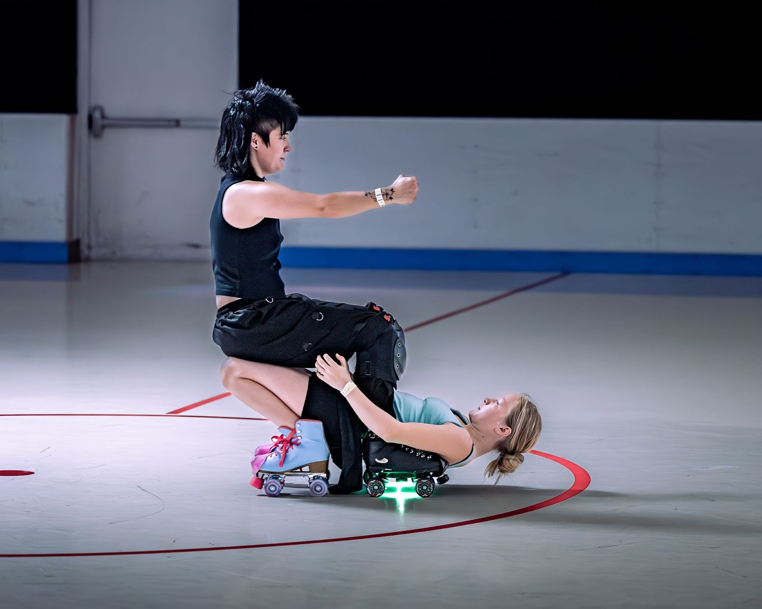 Two roller skaters perform a dramatic artistic routine, with one kneeling over the other on an indoor rink.
