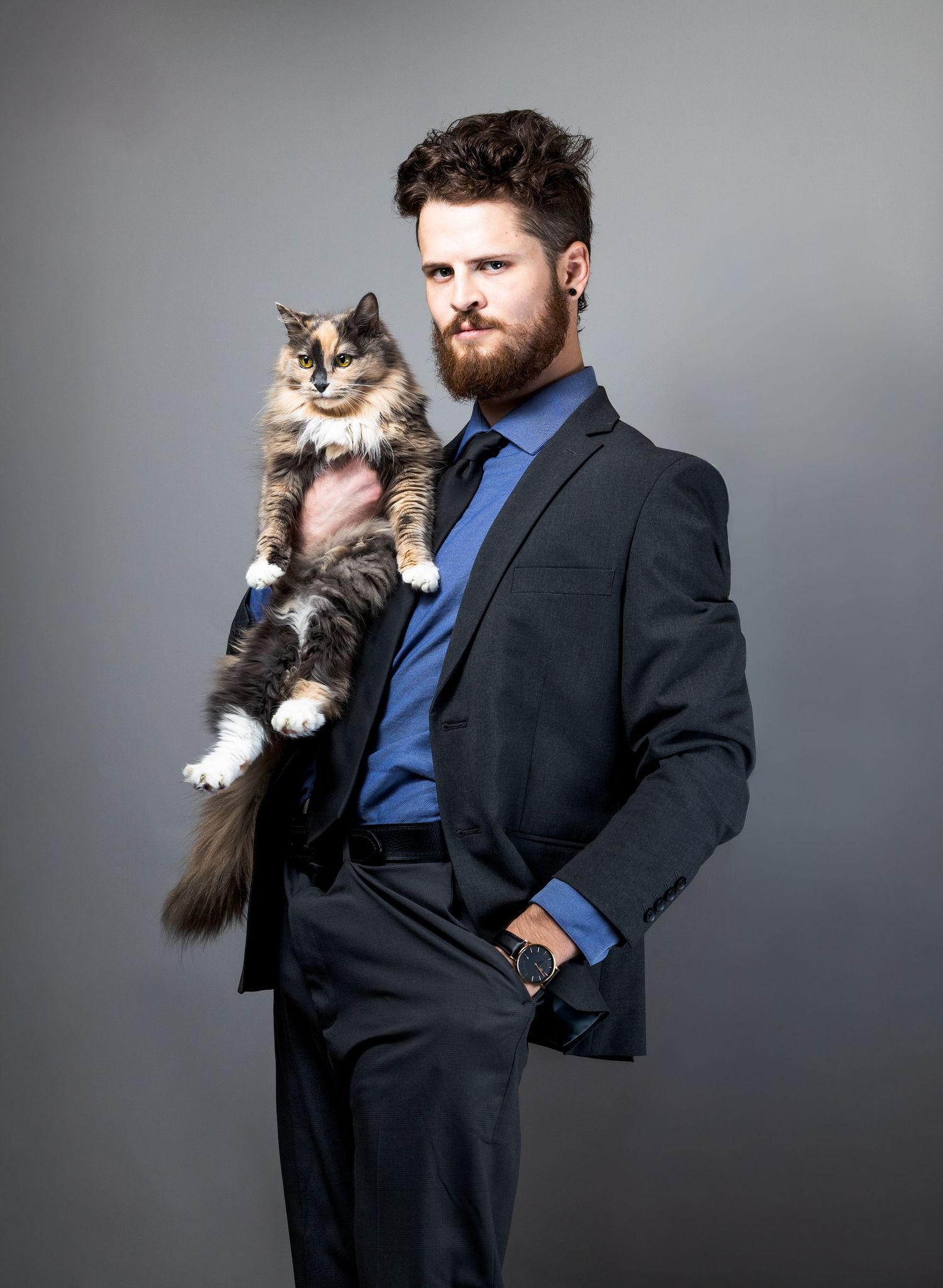 Formal business portrait with calico cat in arms against gray studio background.