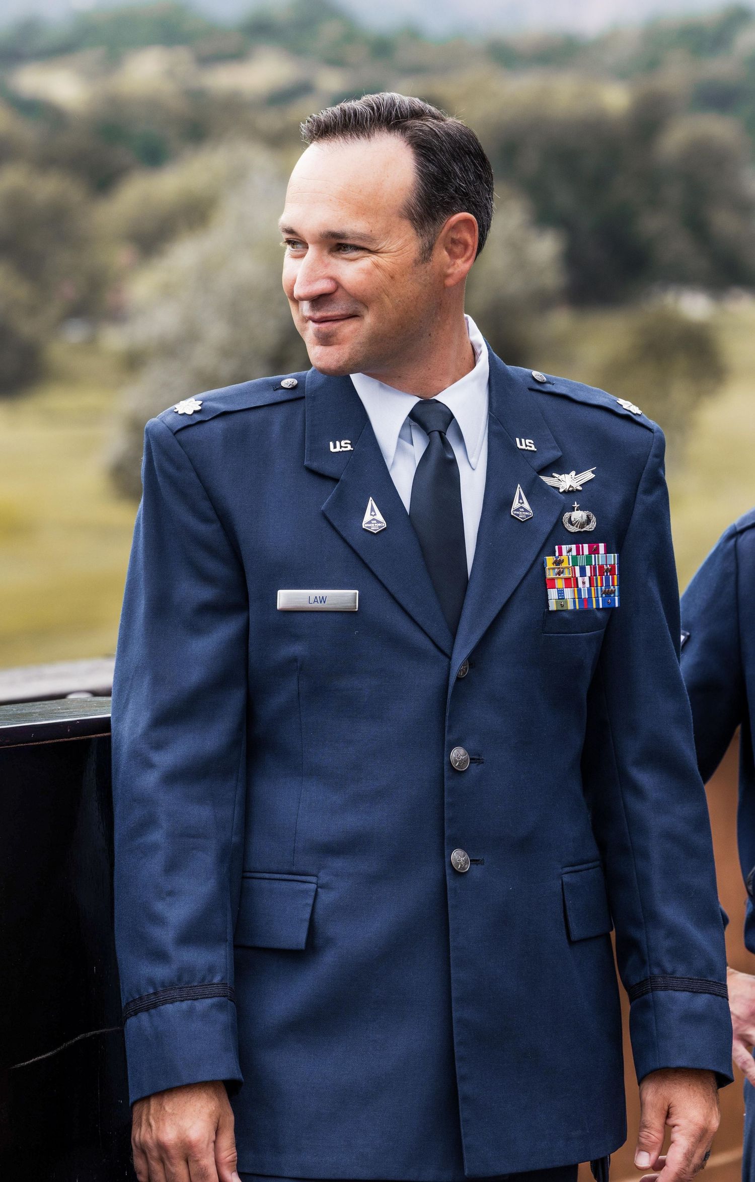 Military service member in dress blues uniform with decorations standing outdoors.
