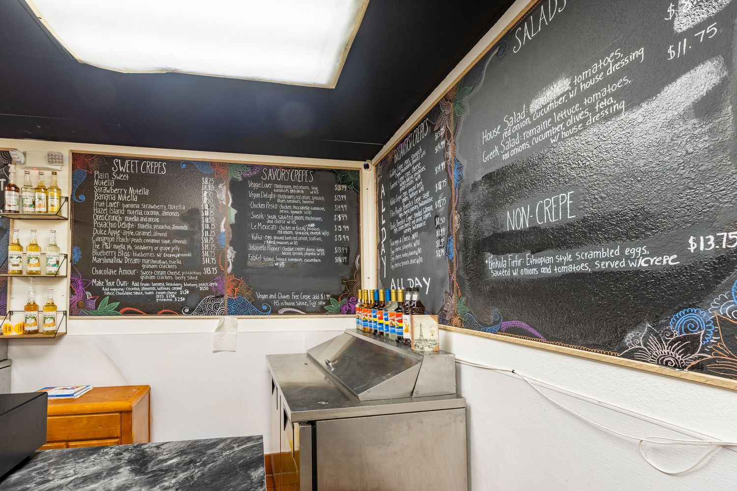 Chalkboard menu wall in a cozy cafe displaying salads, crepes, and daily specials with colorful chalk writing.