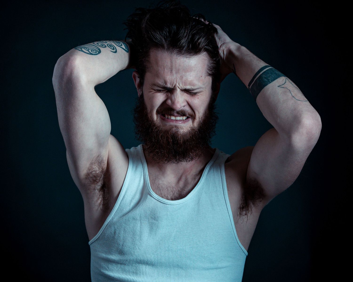A person in a white tank top shows expressions of pain and discomfort against a dark background in a photo series.