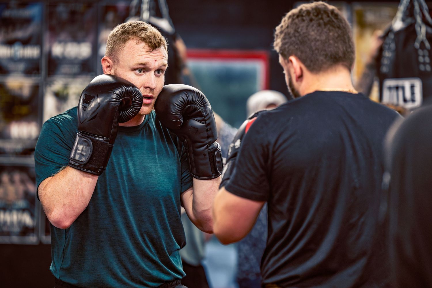 Two boxers spar in a training session wearing protective gloves and athletic wear.