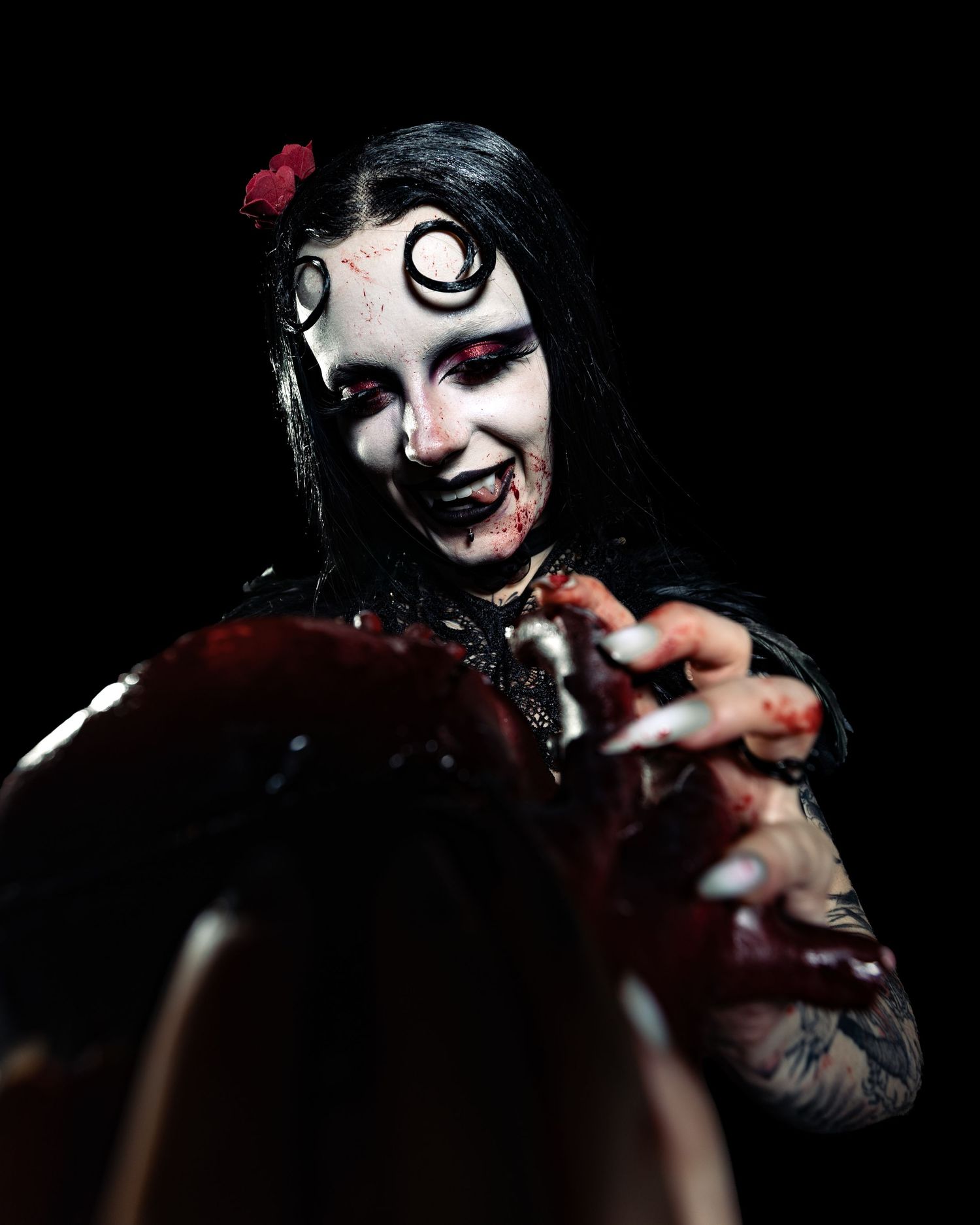 Dramatic horror makeup with spiral eye design, blood effects, and tattoos in dark studio portrait.