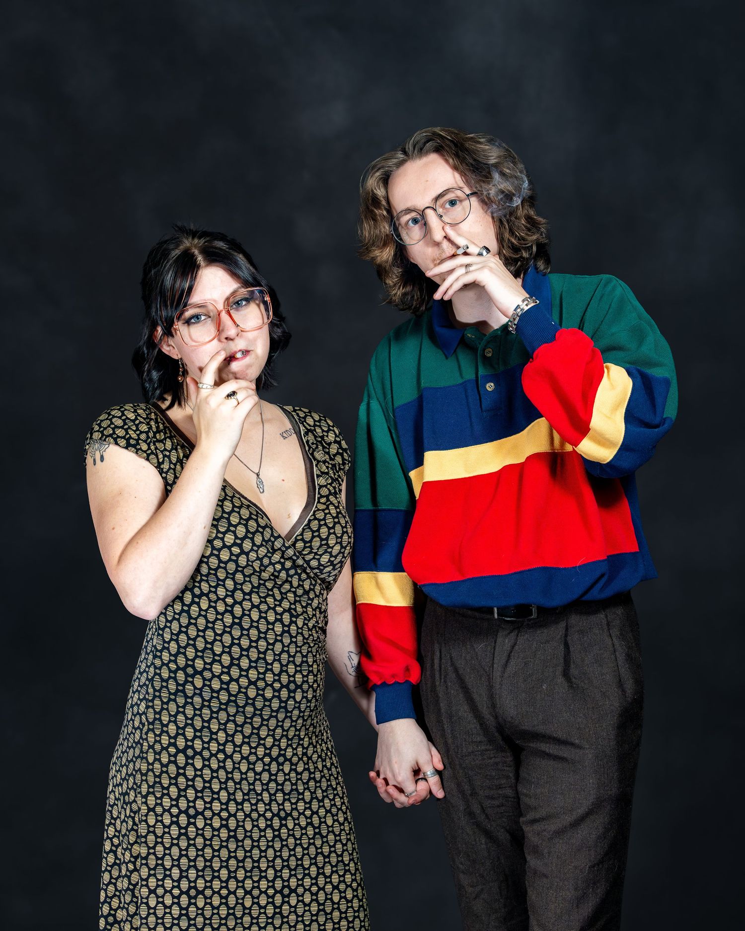 A couple posing thoughtfully with hands on chins, wearing colorful sweater and green floral dress.