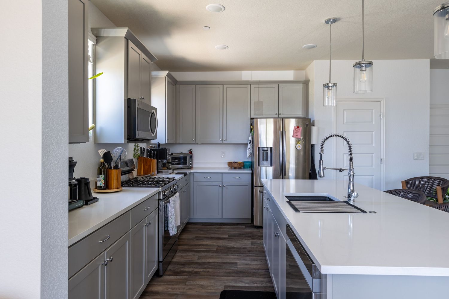 Modern kitchen with gray cabinets, stainless steel appliances, white island with sink, and pendant lighting.